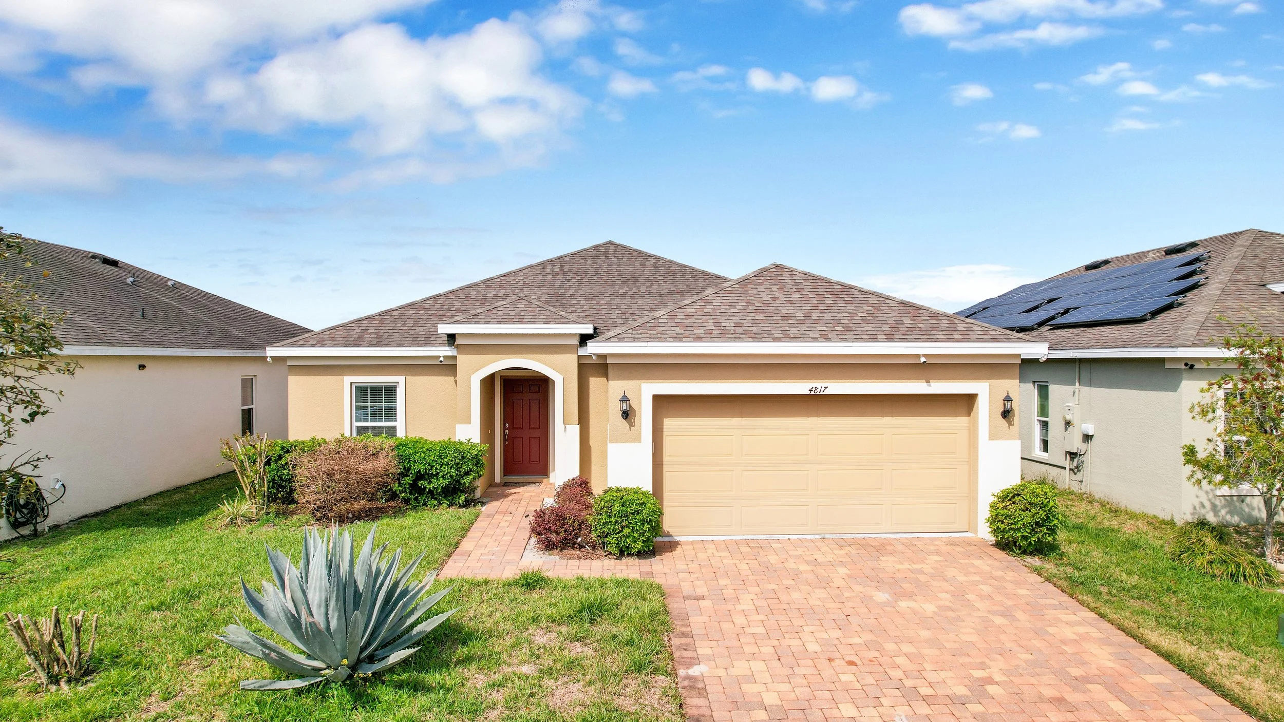 Modern two-story house with blue siding, a blue garage door, and a small front porch, surrounded by a landscaped yard with palm trees and bushes.