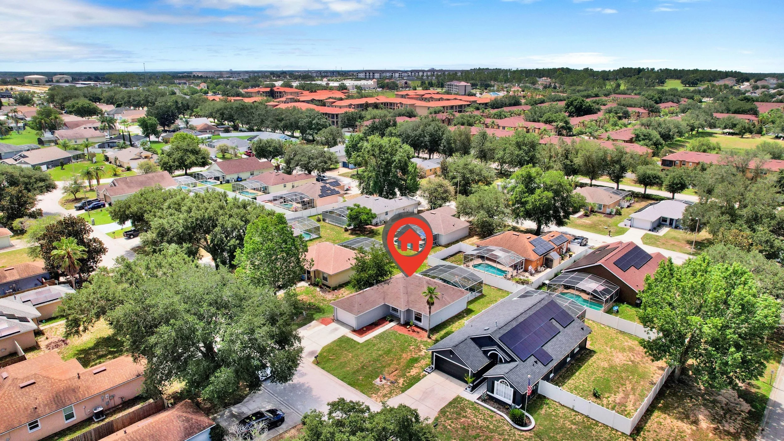 Aerial view of a suburban neighborhood with houses, trees, and swimming pools, featuring a red location marker pointing to a specific house.