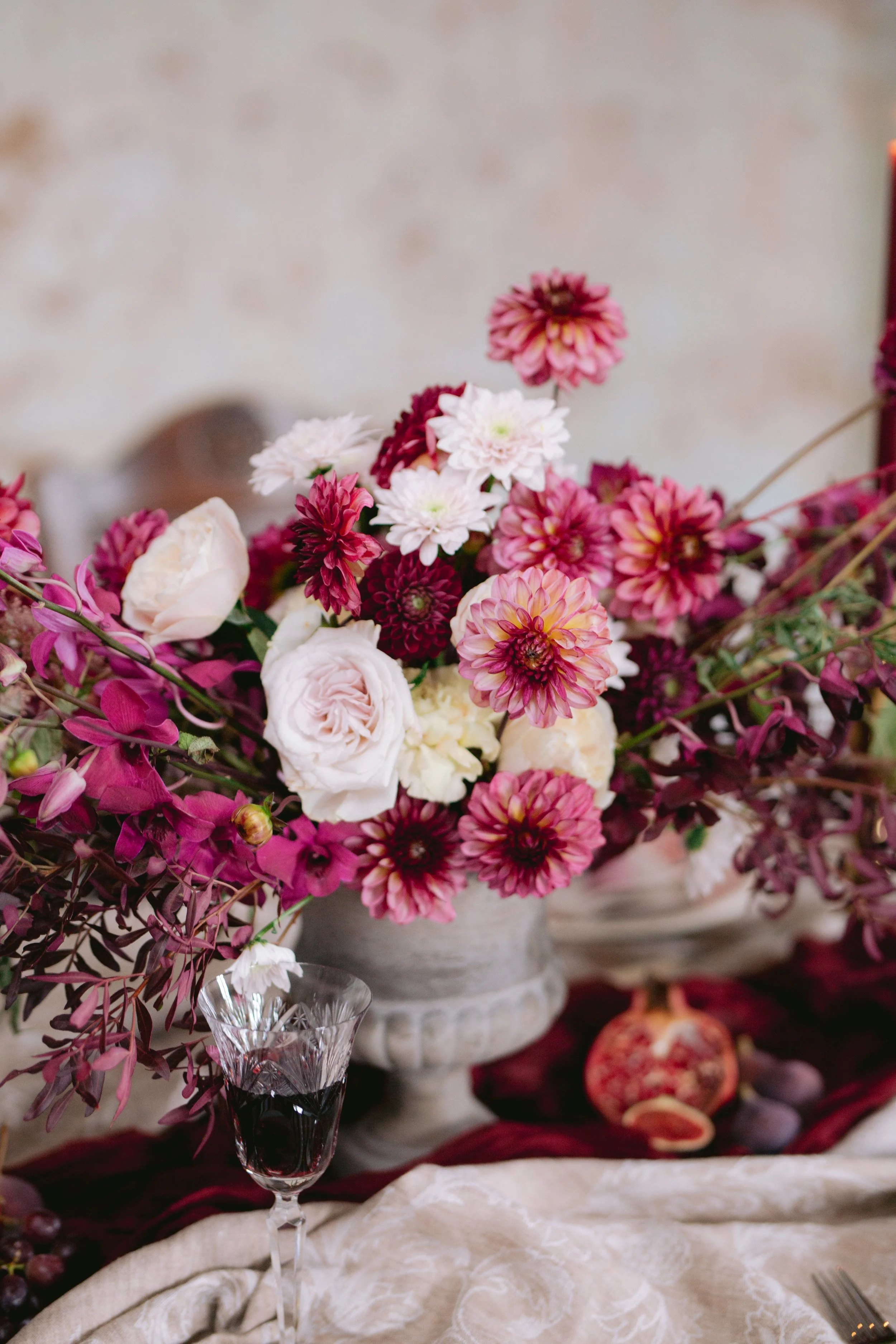Blumenstrauß mit rosa, weißen und burgunderfarbenen Blumen in einer grauen Vase auf einem festlich gedeckten Tisch.