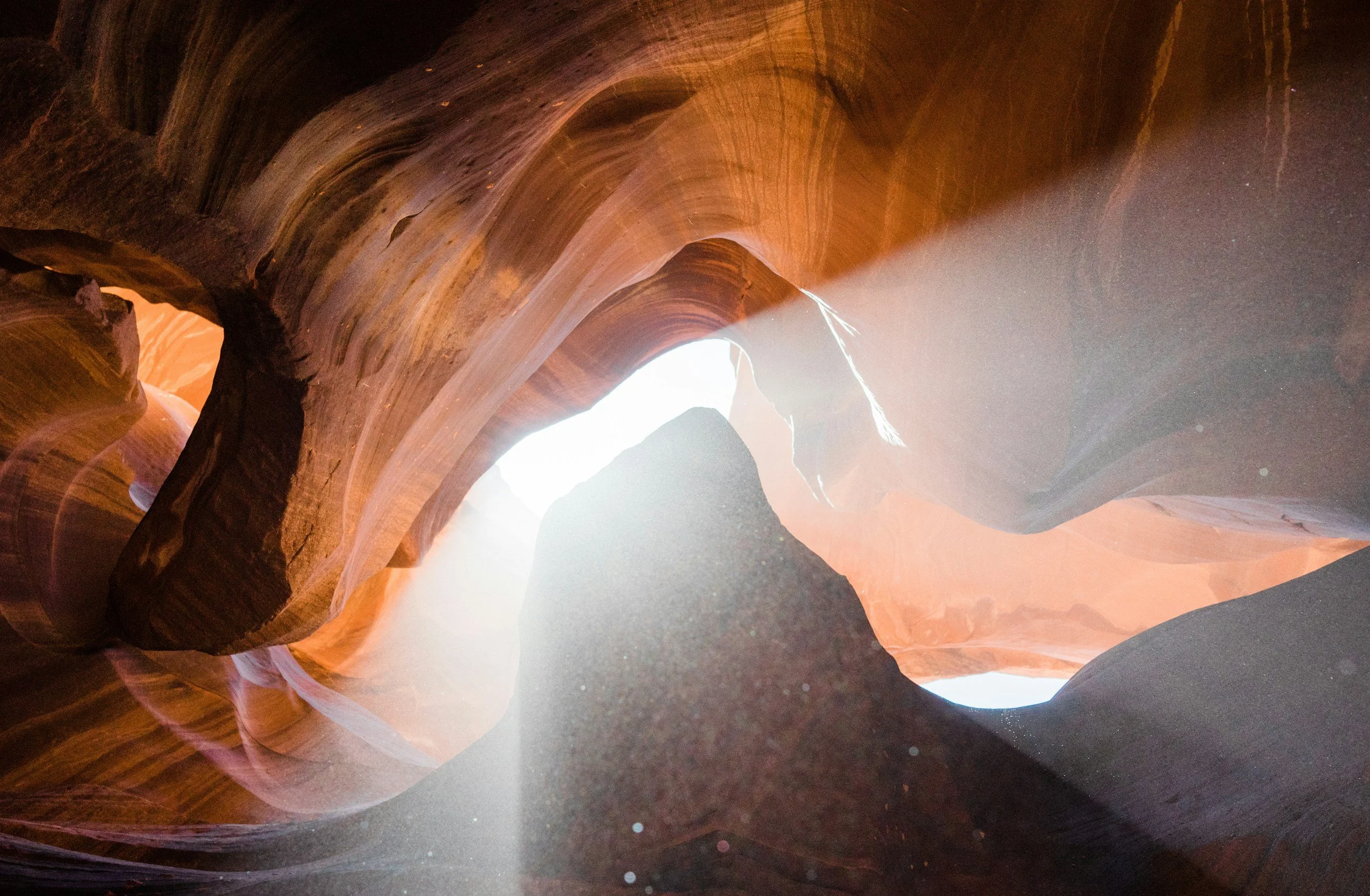 Sunlight illuminating the inside of a narrow, winding canyon with smooth, layered rock walls in shades of orange and brown.
