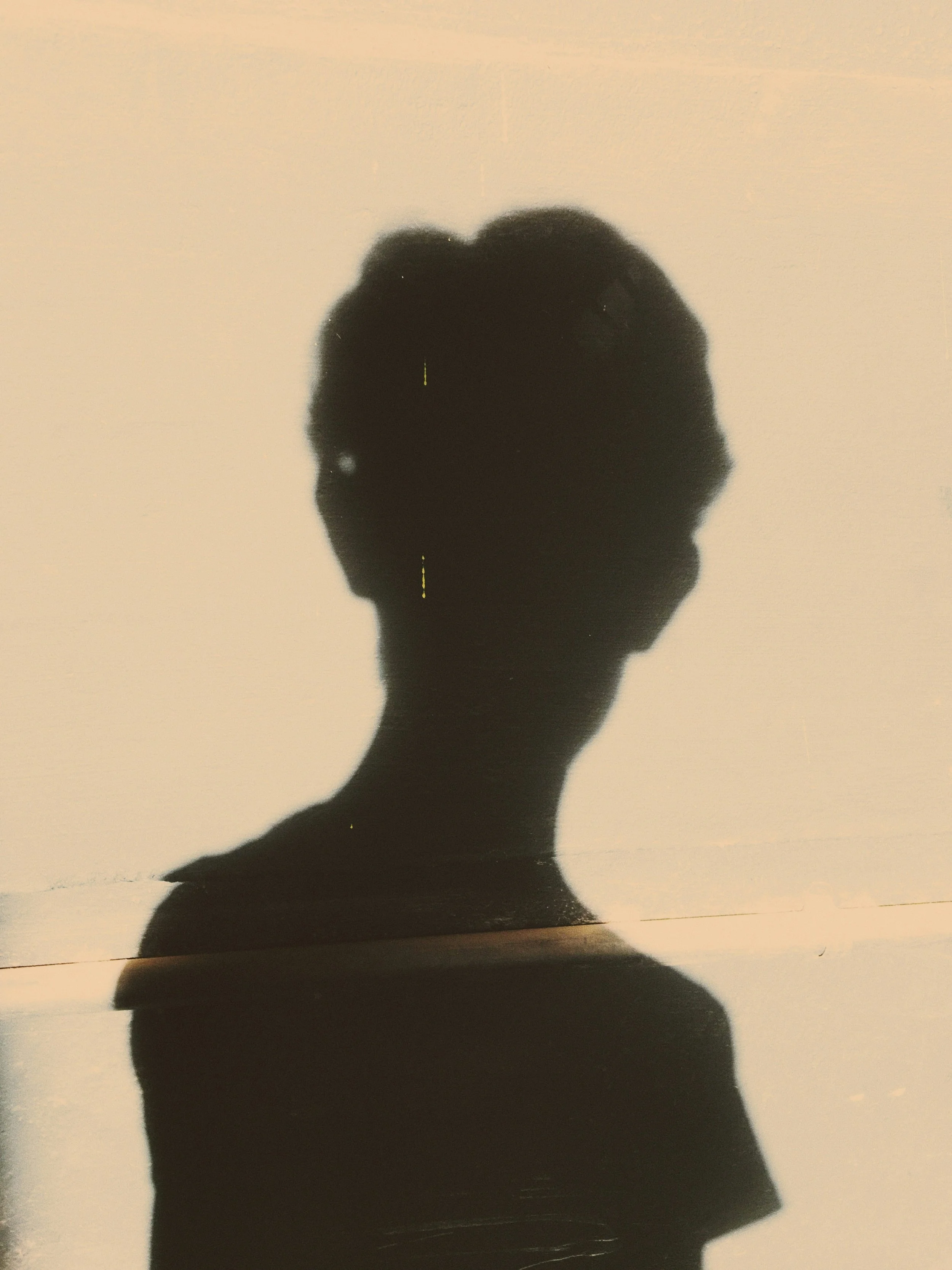Silhouette of a person's head and shoulders, cast as a shadow on a light background.