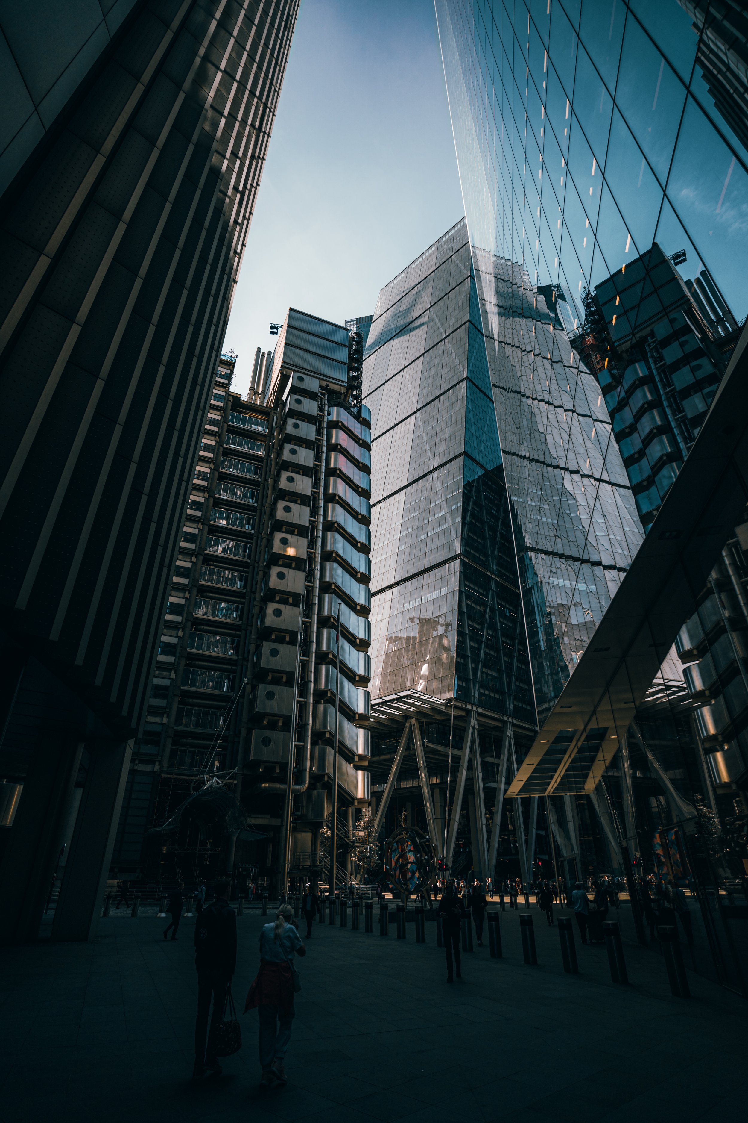Skyscrapers with reflective glass facades in an urban city, with pedestrians walking on the sidewalk below.