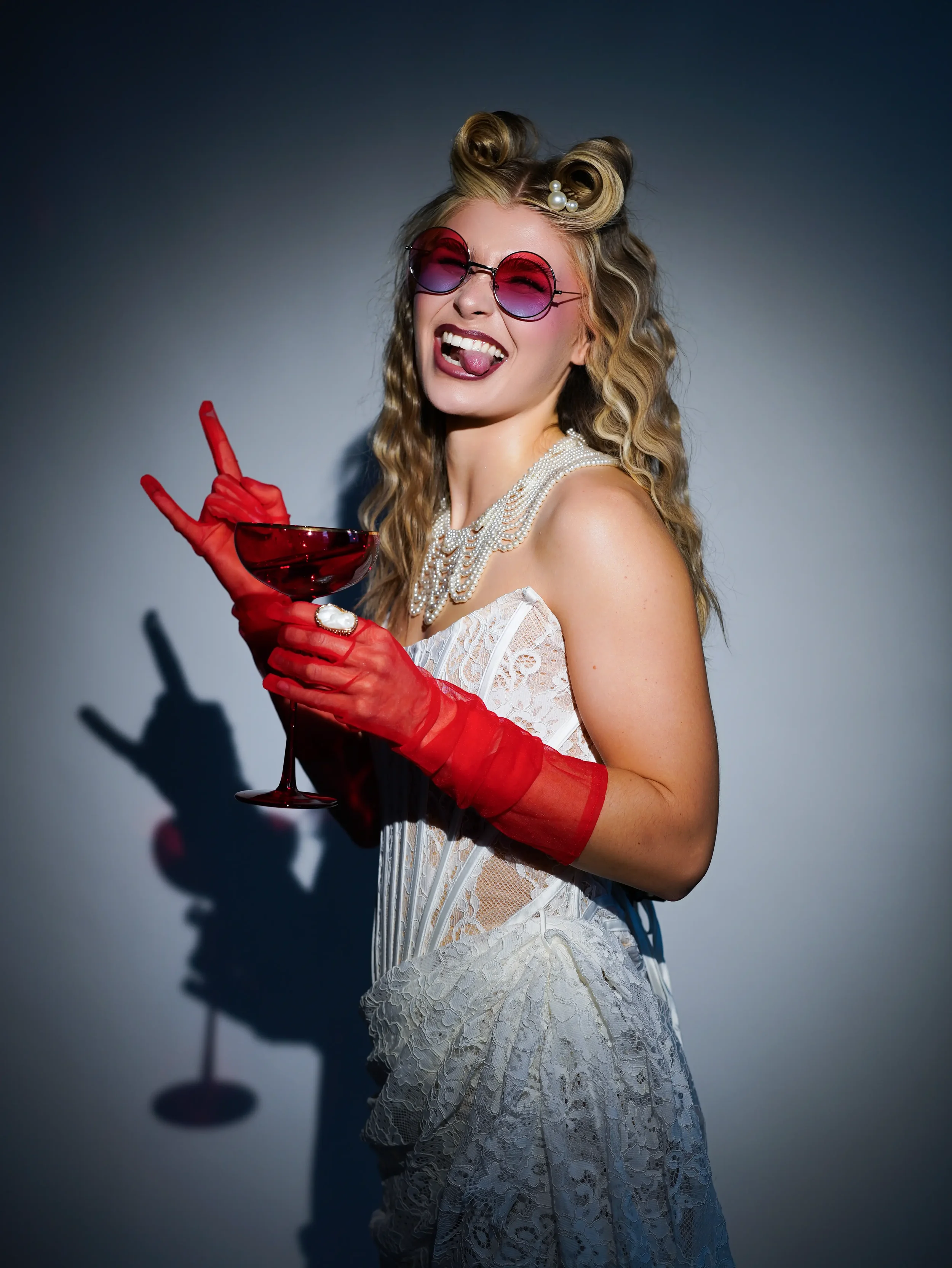 Woman in lace corset and red gloves holding martini glass, bold editorial fashion portrait New Moon Agency Klagenfurt