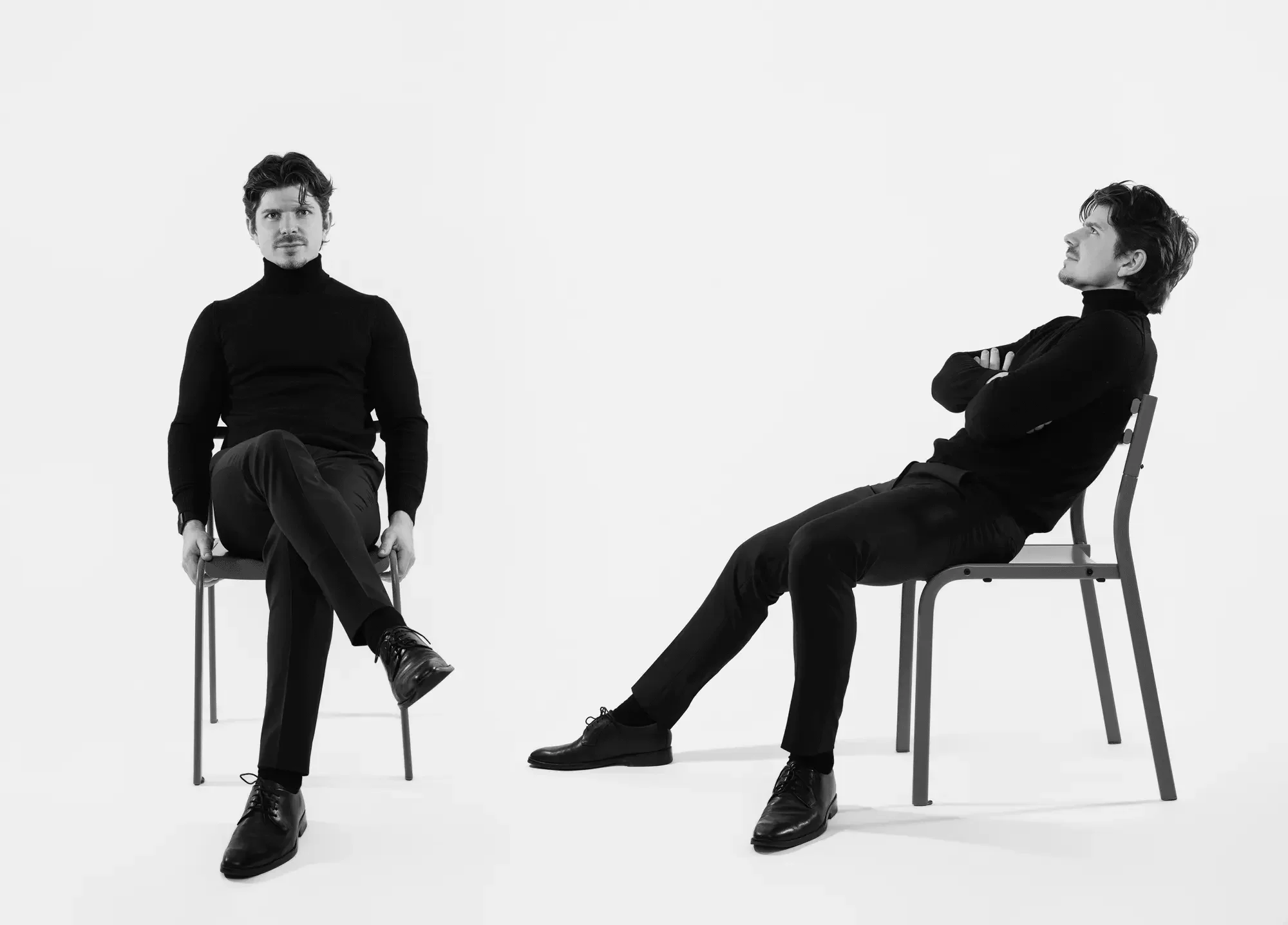 Two men in black turtlenecks seated on chairs in contrasting poses, studio portrait photography New Moon Agency Klagenfurt
