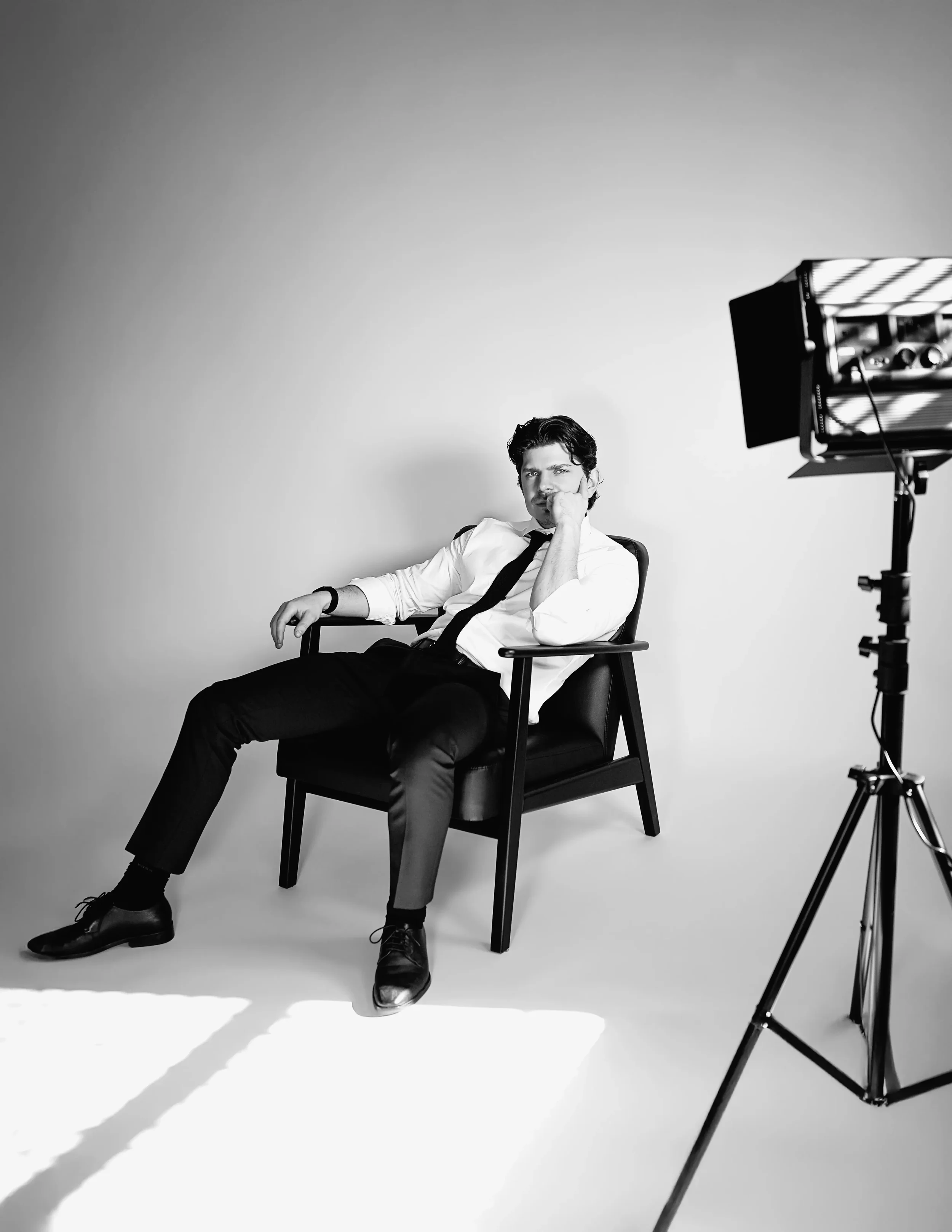 Black and white studio portrait of man in shirt and tie seated in armchair, professional portrait photography New Moon Agency Klagenfurt
