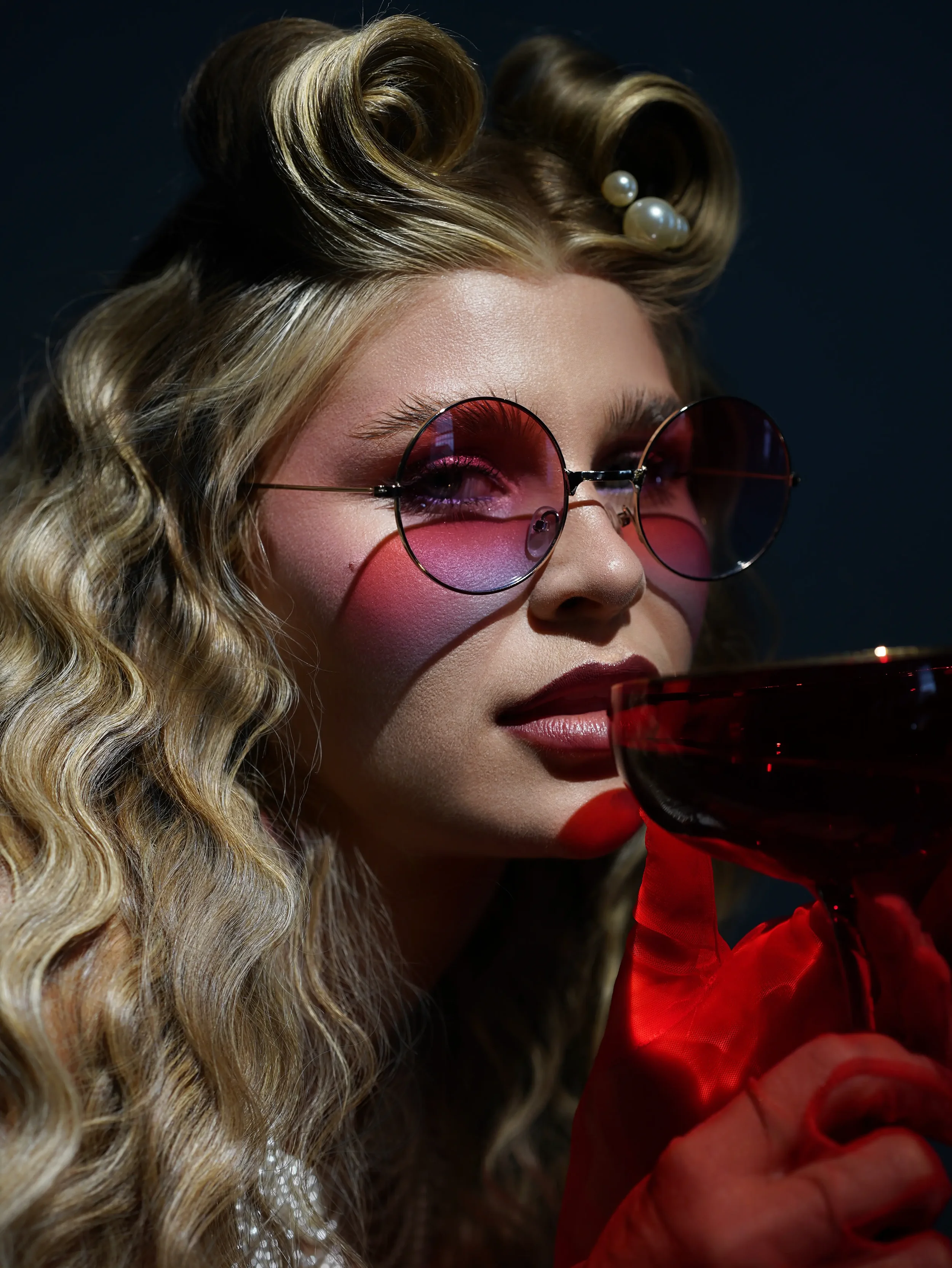 Close-up portrait of woman with vintage curls, round pink sunglasses and red cocktail glass, editorial fashion photography New Moon Agency Klagenfurt