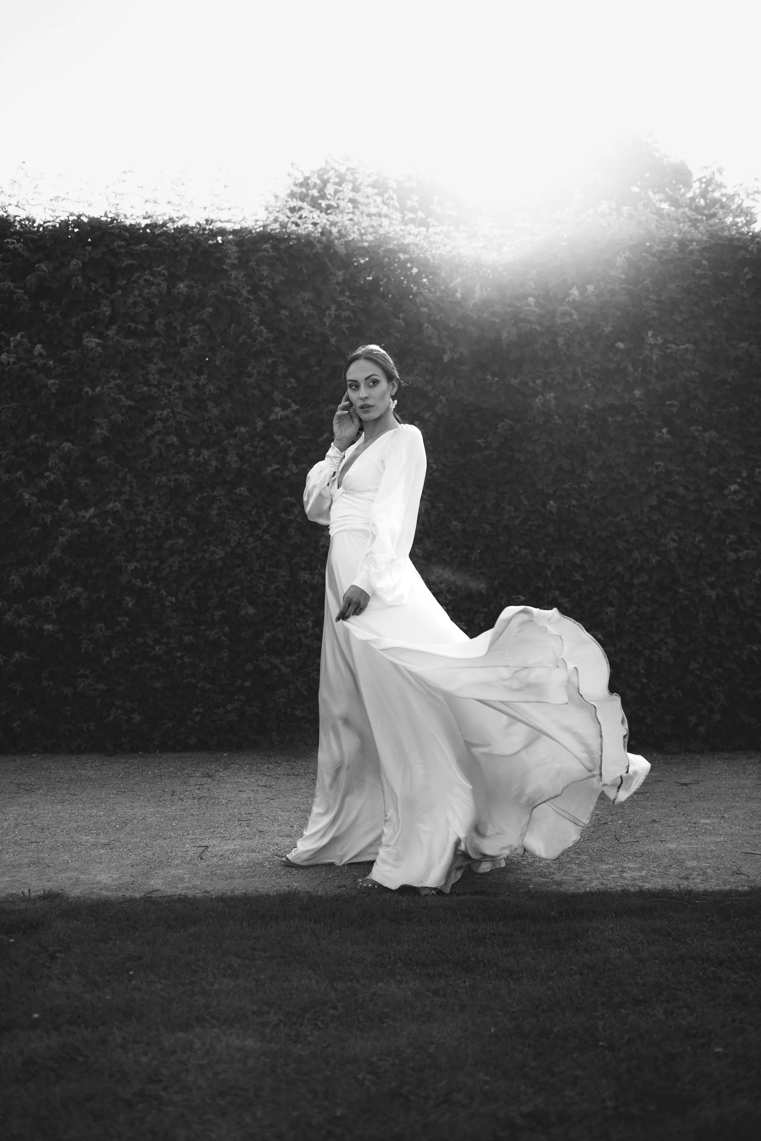 Bride in flowing gown walking through Belvedere’s formal garden in the evening sun