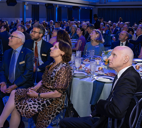 Business professionals attending a formal event or conference in a well-lit room with round tables set with glasses and plates