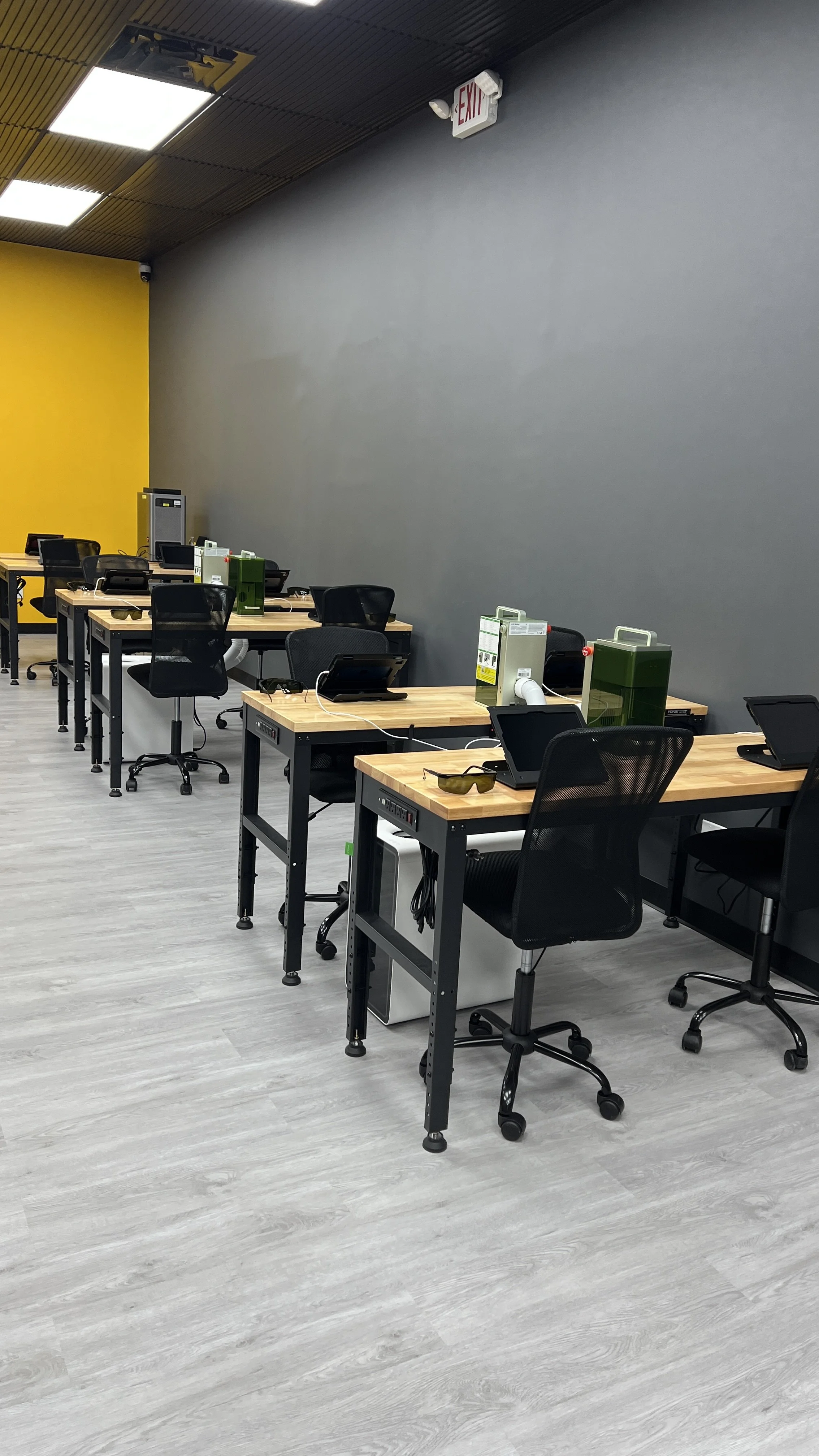 An empty office with wooden desks, black chairs, computers, and partitions in a modern workspace.