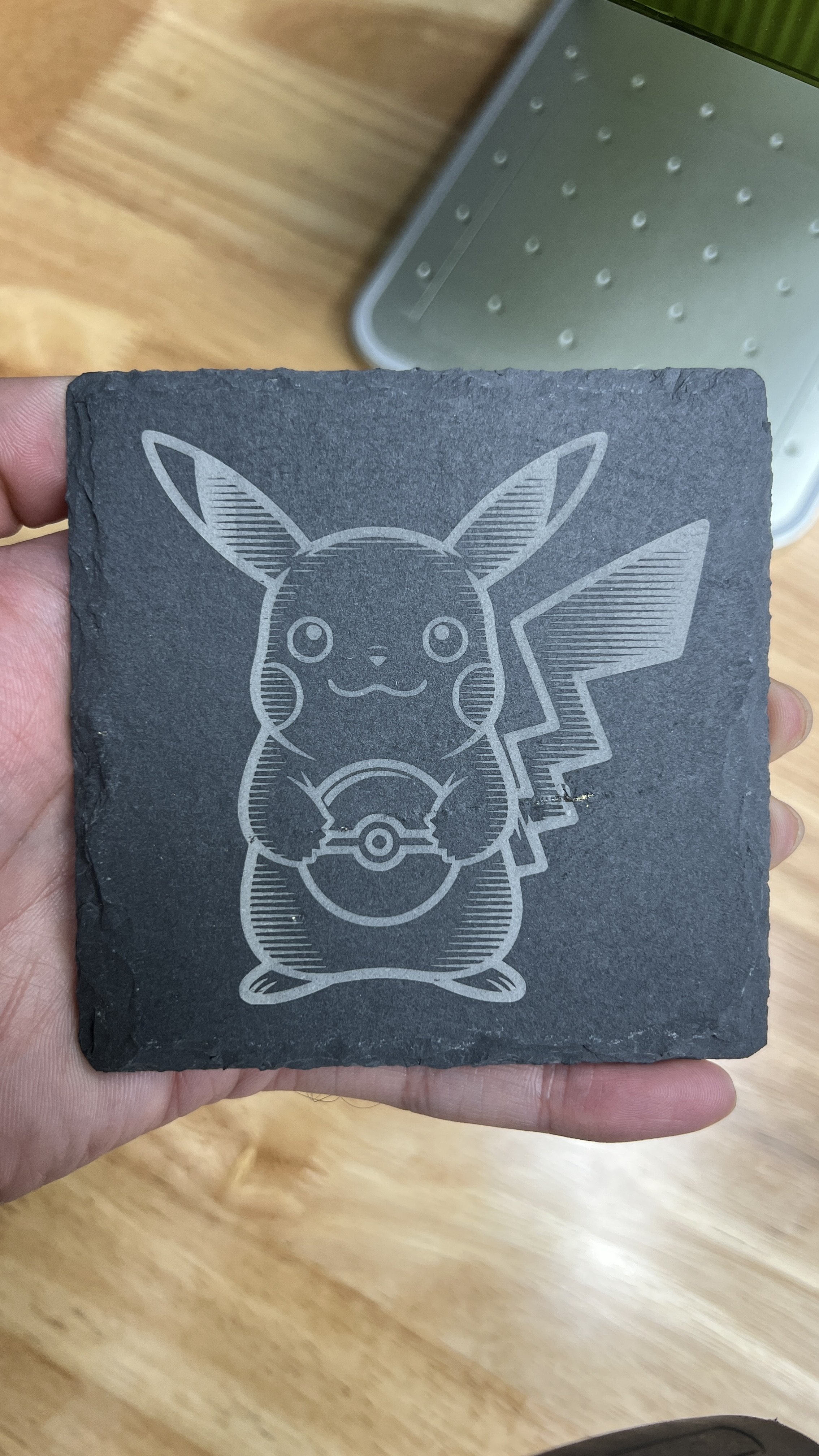 A person holding a black stone tile with an engraved outline of Pikachu holding a Pokéball.