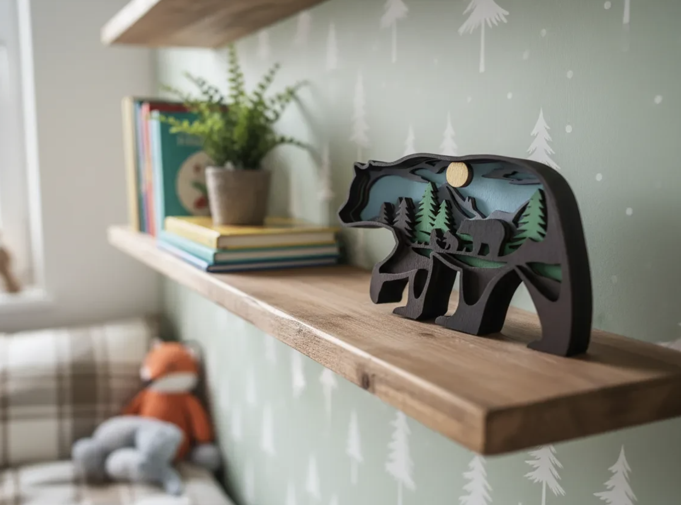 A wooden shelf on a wall with a potted plant, a stack of colorful books, and a decorative black and green mountain and forest scene figurine.