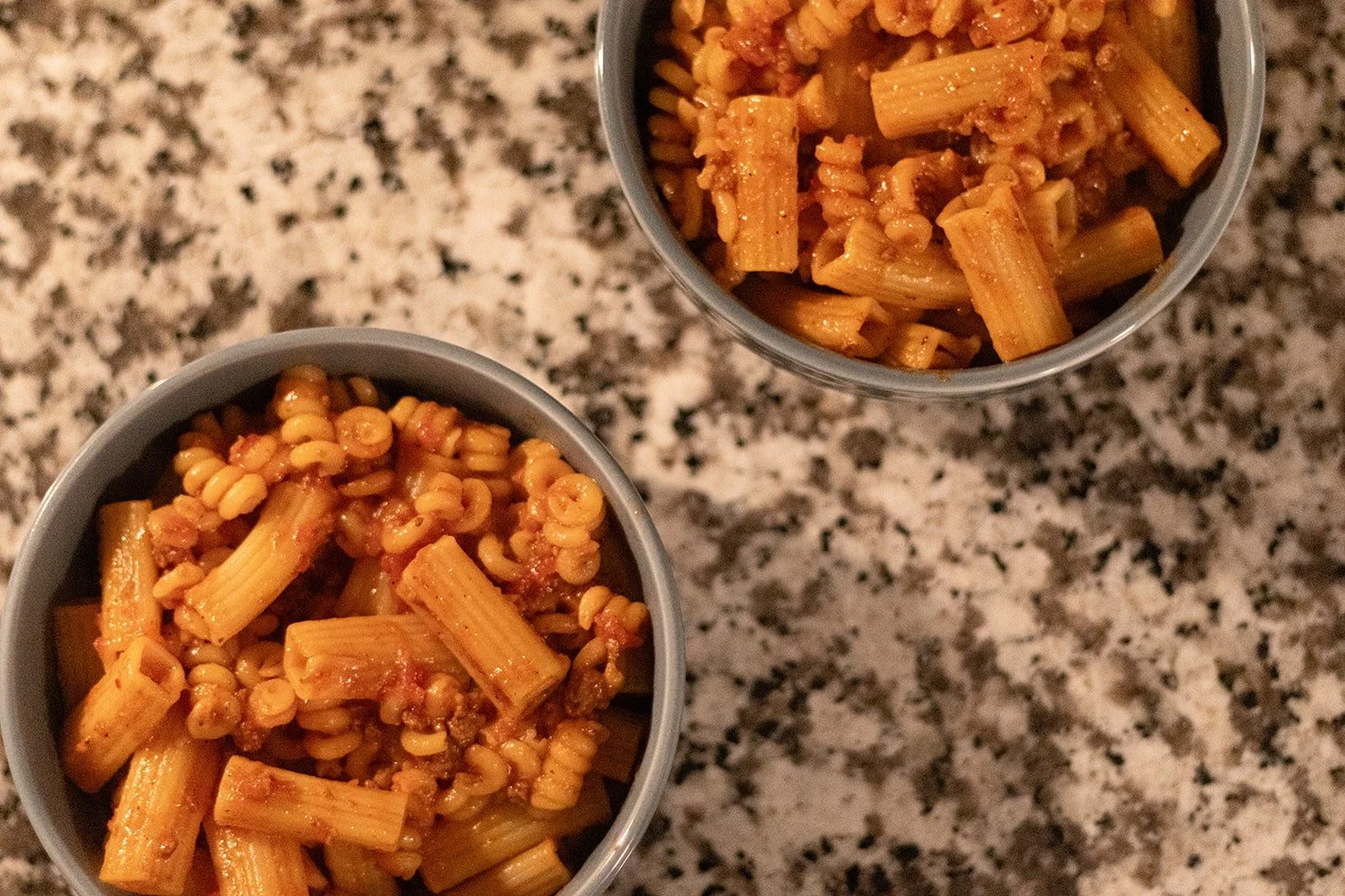 Two cups of cooked pasta with meat sauce on a granite countertop.