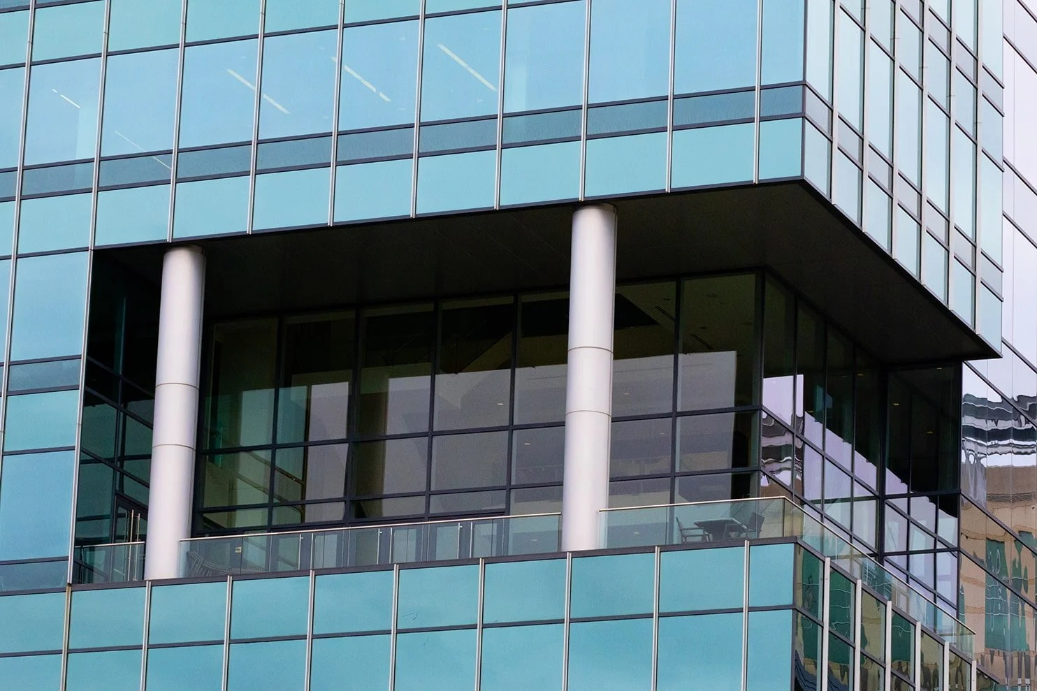 Close-up of a modern glass office building with reflective windows and white support columns.