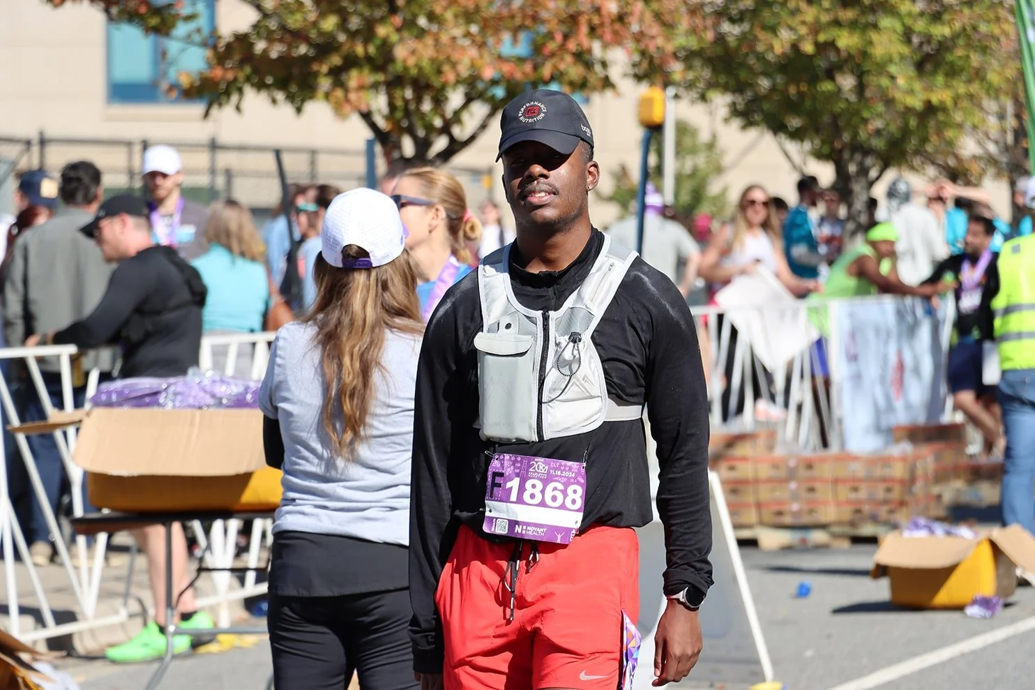 Male marathon runner wearing a black cap, black long-sleeve shirt, red shorts, and a race bib number 1868 at a race event.
