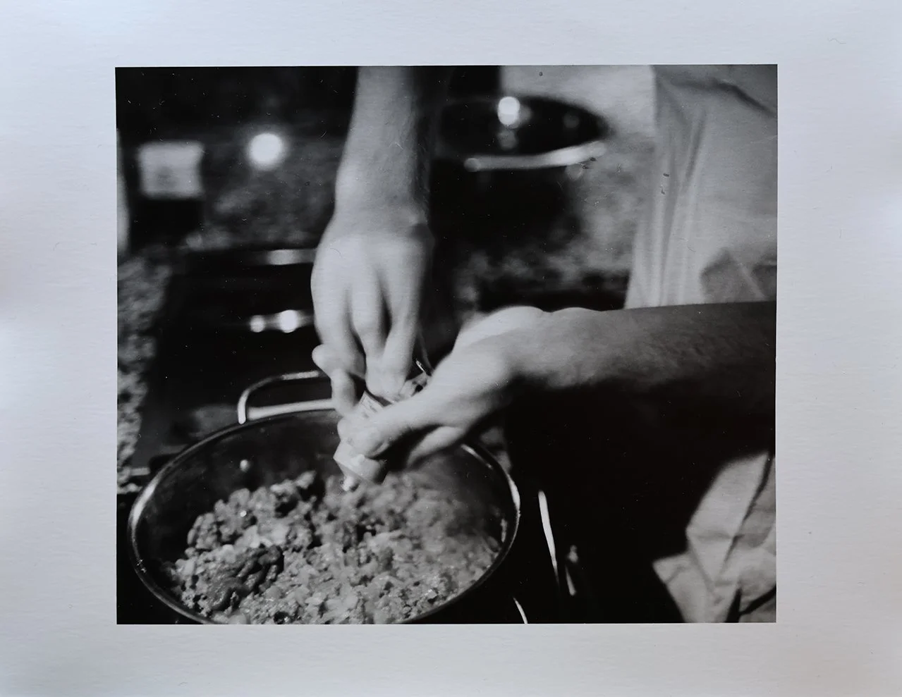 Close-up of hands adding seasoning to a pot of cooked food on a stovetop in a kitchen.