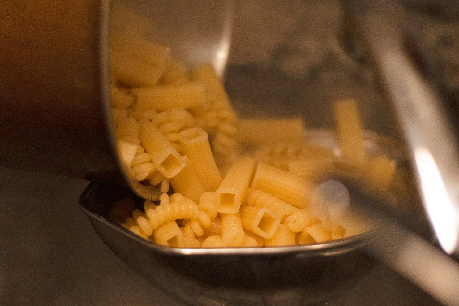 Uncooked pasta being poured from a bag into a pan.