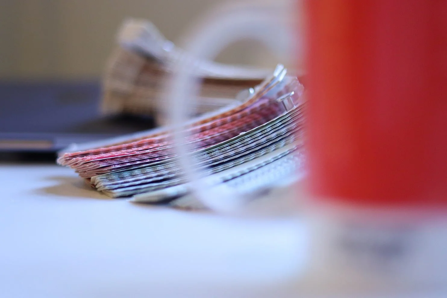 Close-up of a stack of colorful paper currency, slightly out of focus, with a blurred red object on the right.