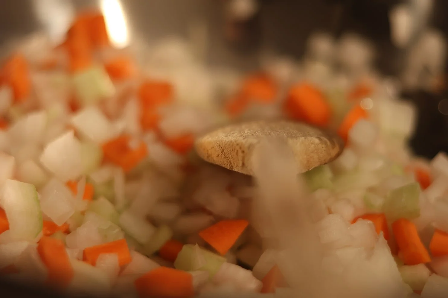 Chopped onions, carrots, and celery being cooked in a pan, with a spoon stirring the mixture.