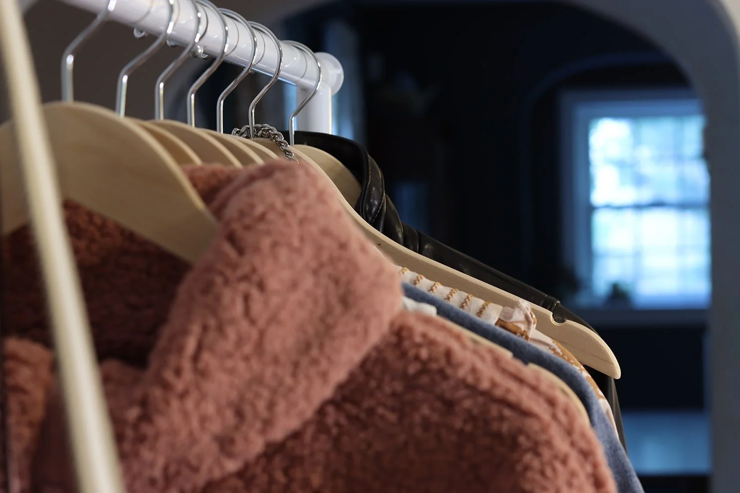 Clothes hanging on a clothing rack, including a pink fuzzy garment and other clothing items.