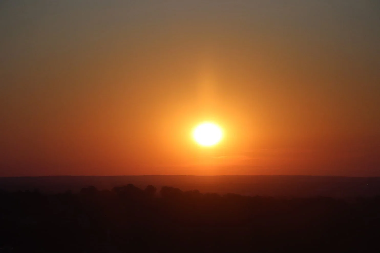 A bright sun setting or rising over a dark landscape with a colorful sky.