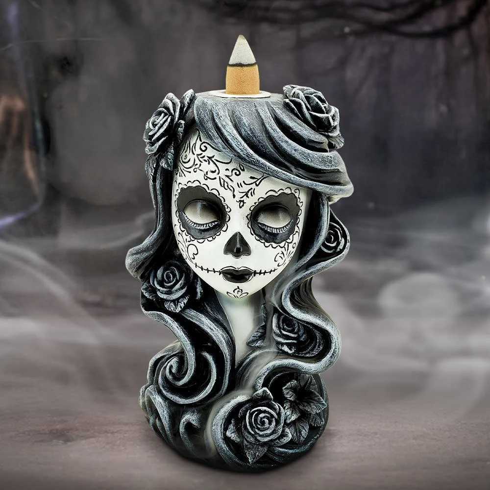 A decorative skull-shaped candle with a woman's face painted in sugar skull style, featuring black and white floral designs, with her long, curled hair decorated with roses, and a large candle wick on top of her head.