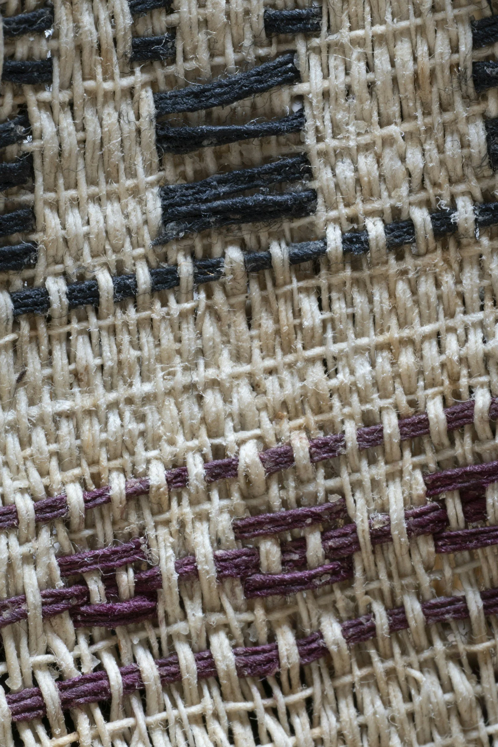 Close-up of woven fabric with beige, black, and maroon threads.