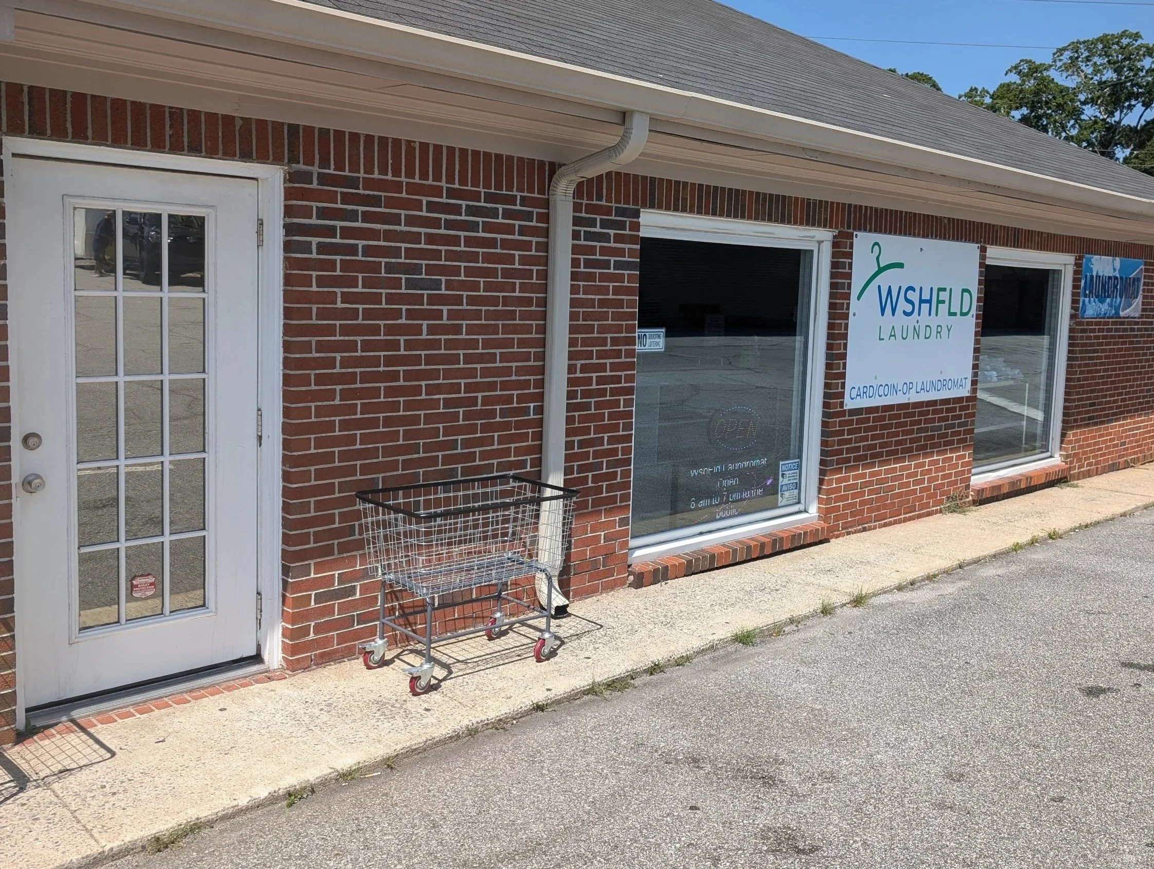 A brick laundromat building with a white door, large front window, and signage for WSHFLD Laundry on Macon Road in Columbus, GA.