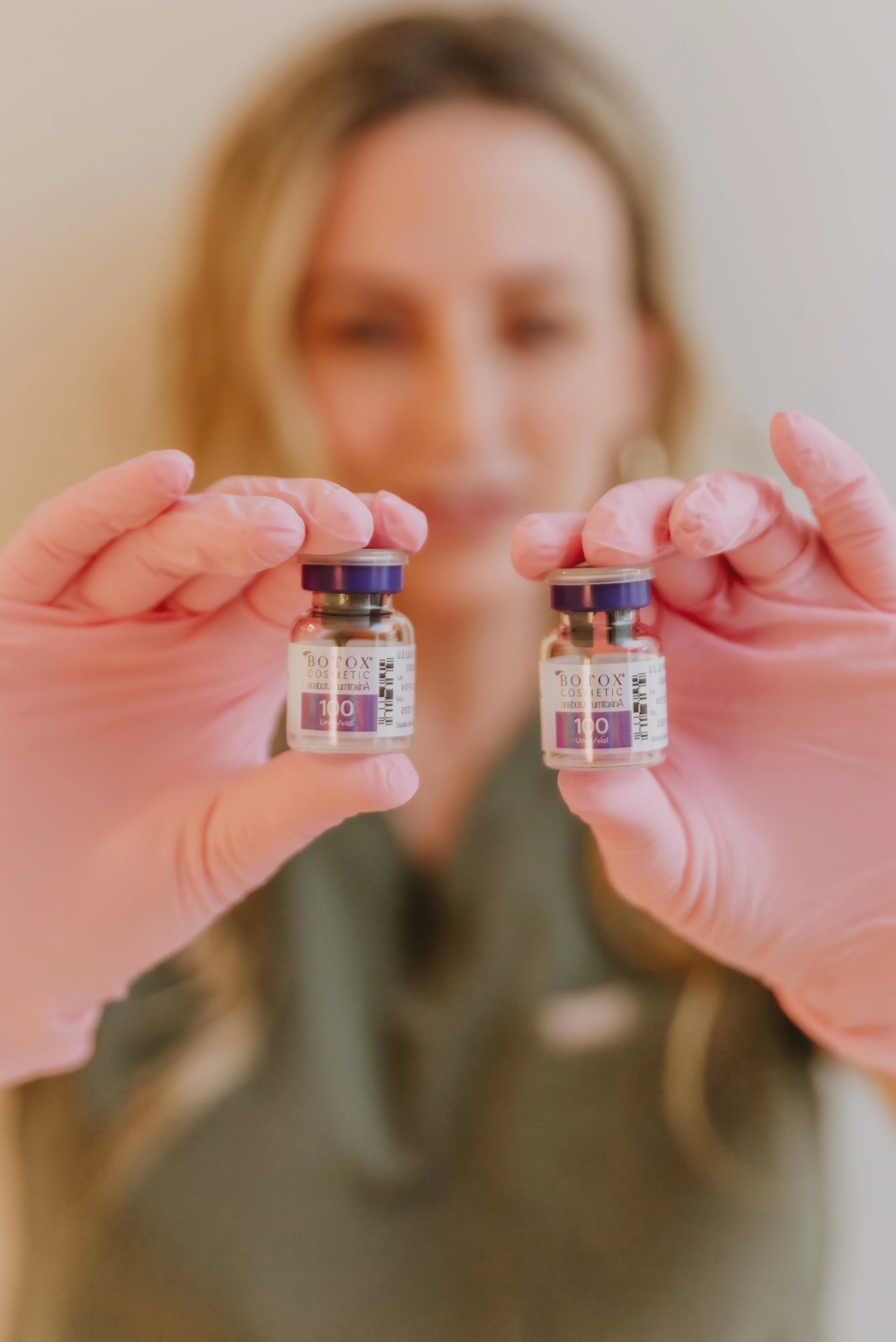 Woman wearing pink gloves holding two small vials labeled botox in front of her face.