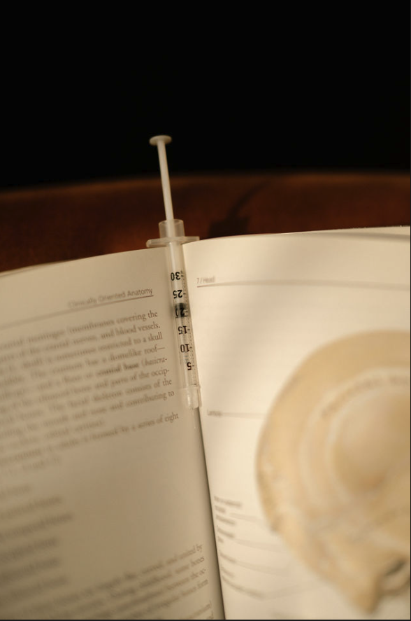 Open medical book with a syringe inserted between the pages and a brown background.