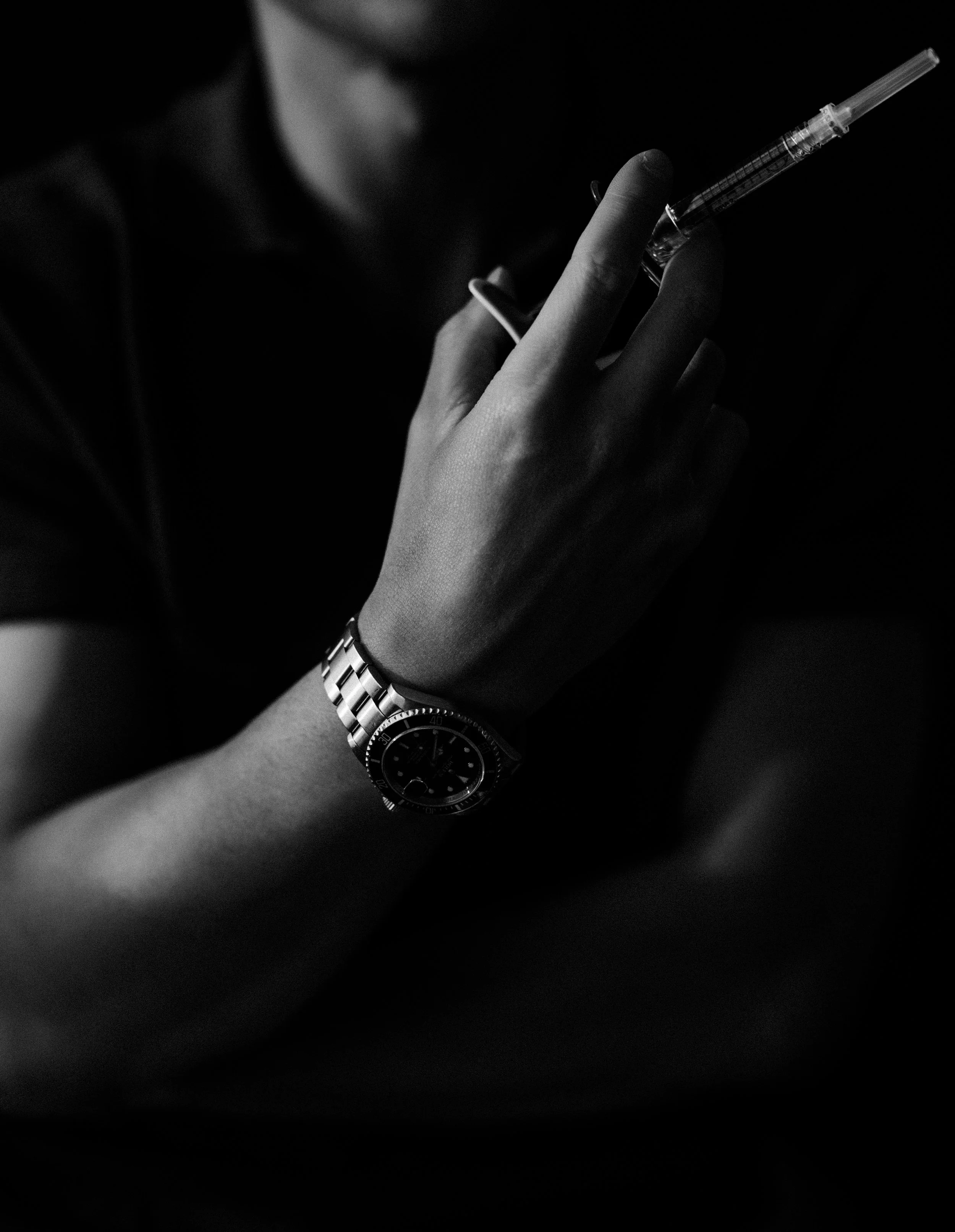 Close-up of a person holding a syringe, wearing a watch on their wrist, with partial facial features visible in the background.