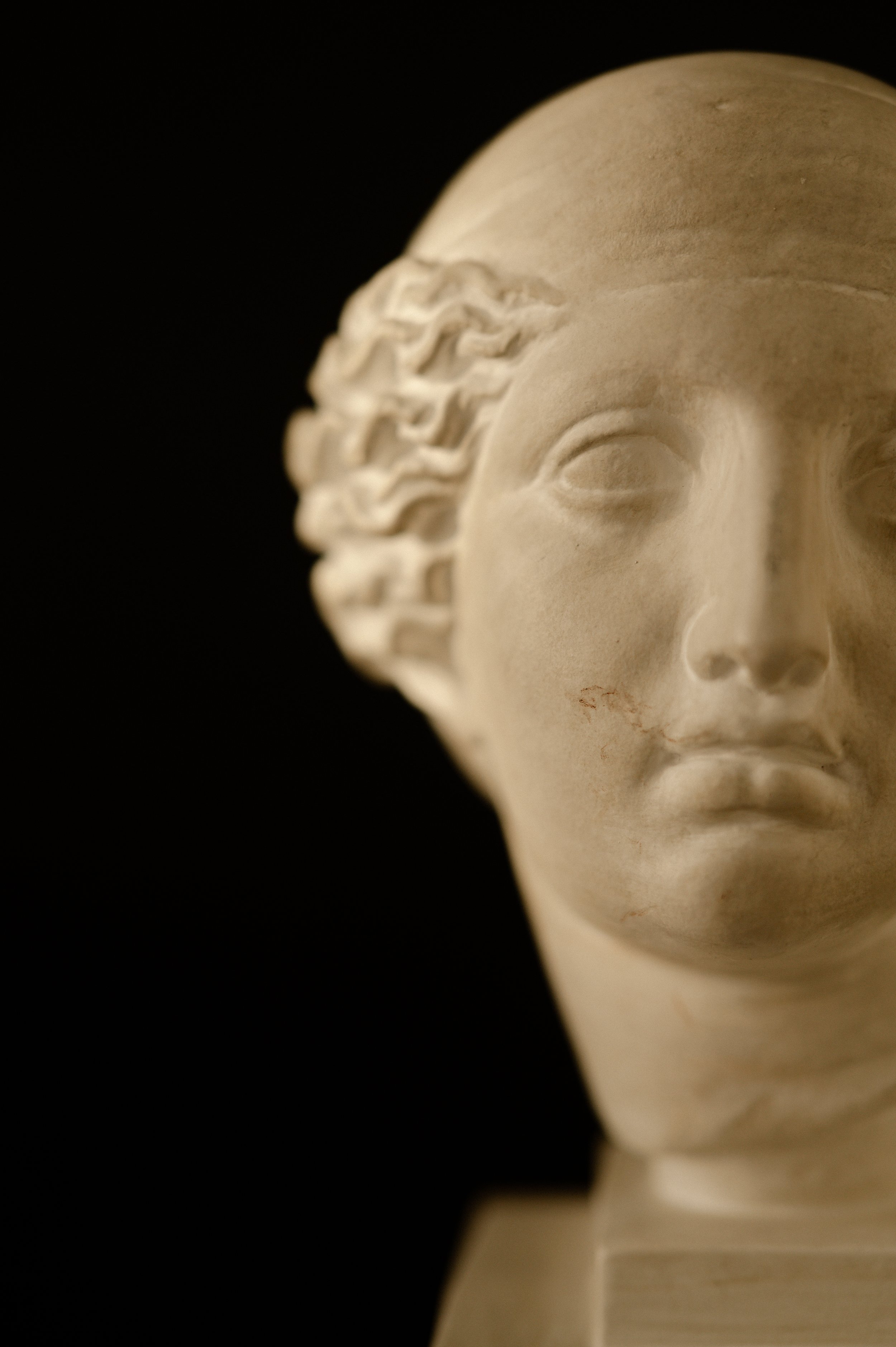 Close-up of a classical marble bust sculpture of a woman's face against a black background.
