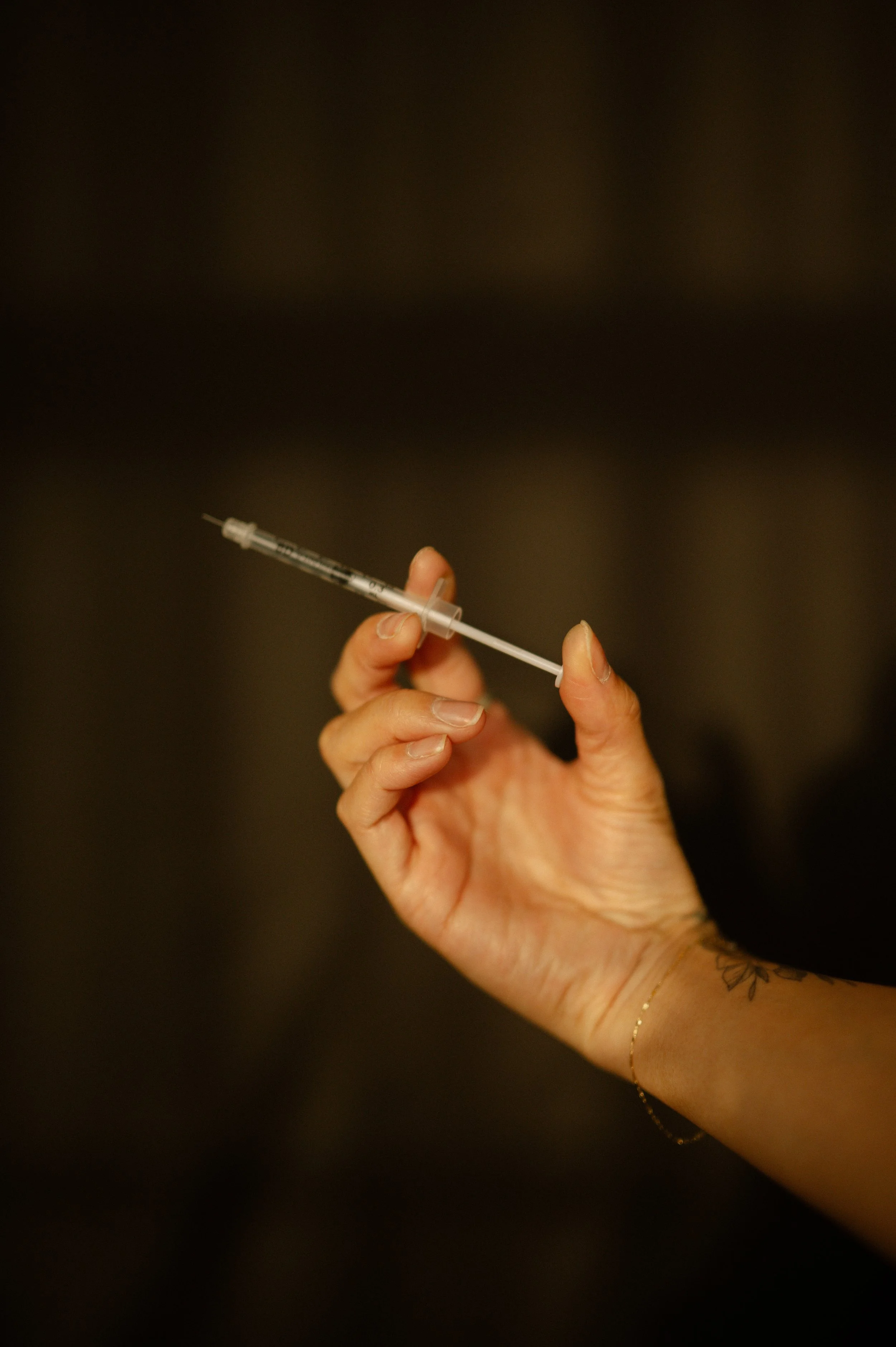 Close-up of a hand holding a syringe, with a dark blurred background.