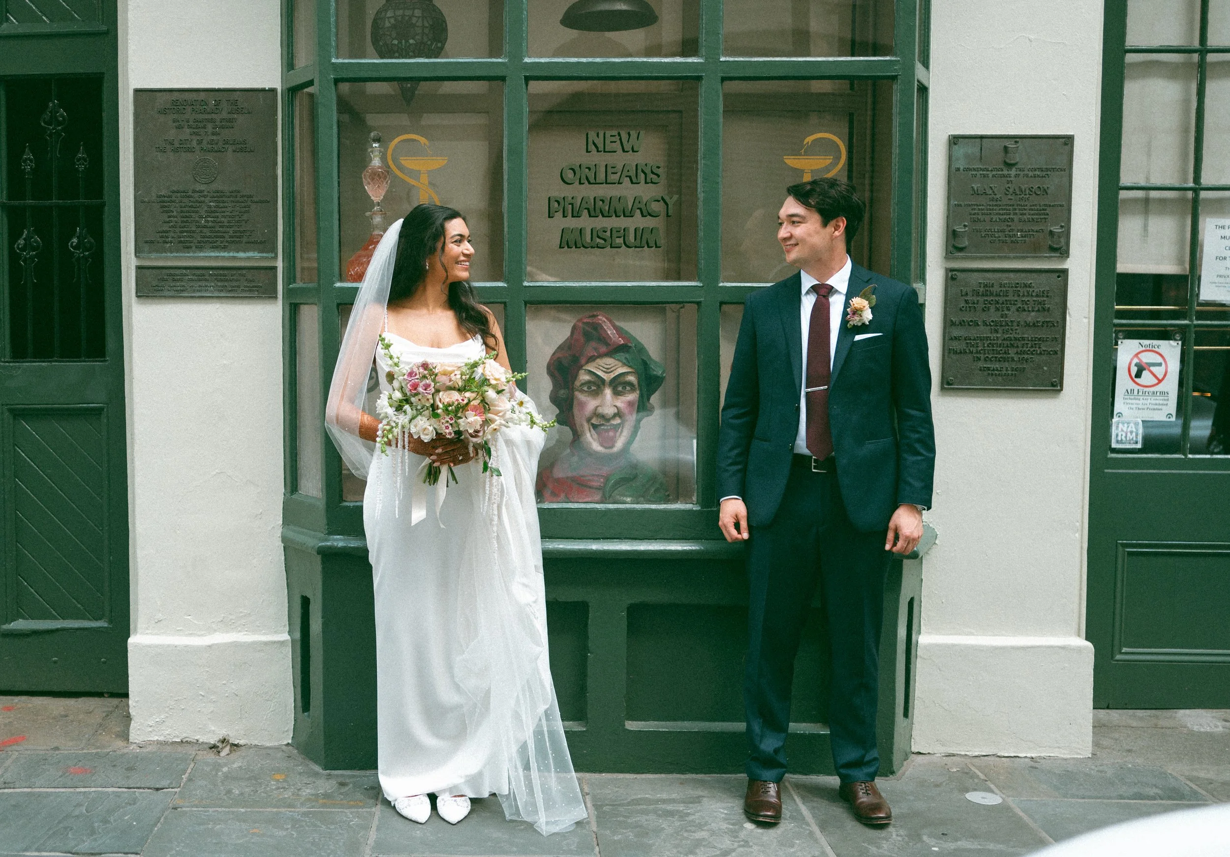A bride and groom standing together looking at one another outside of a museum on the street.