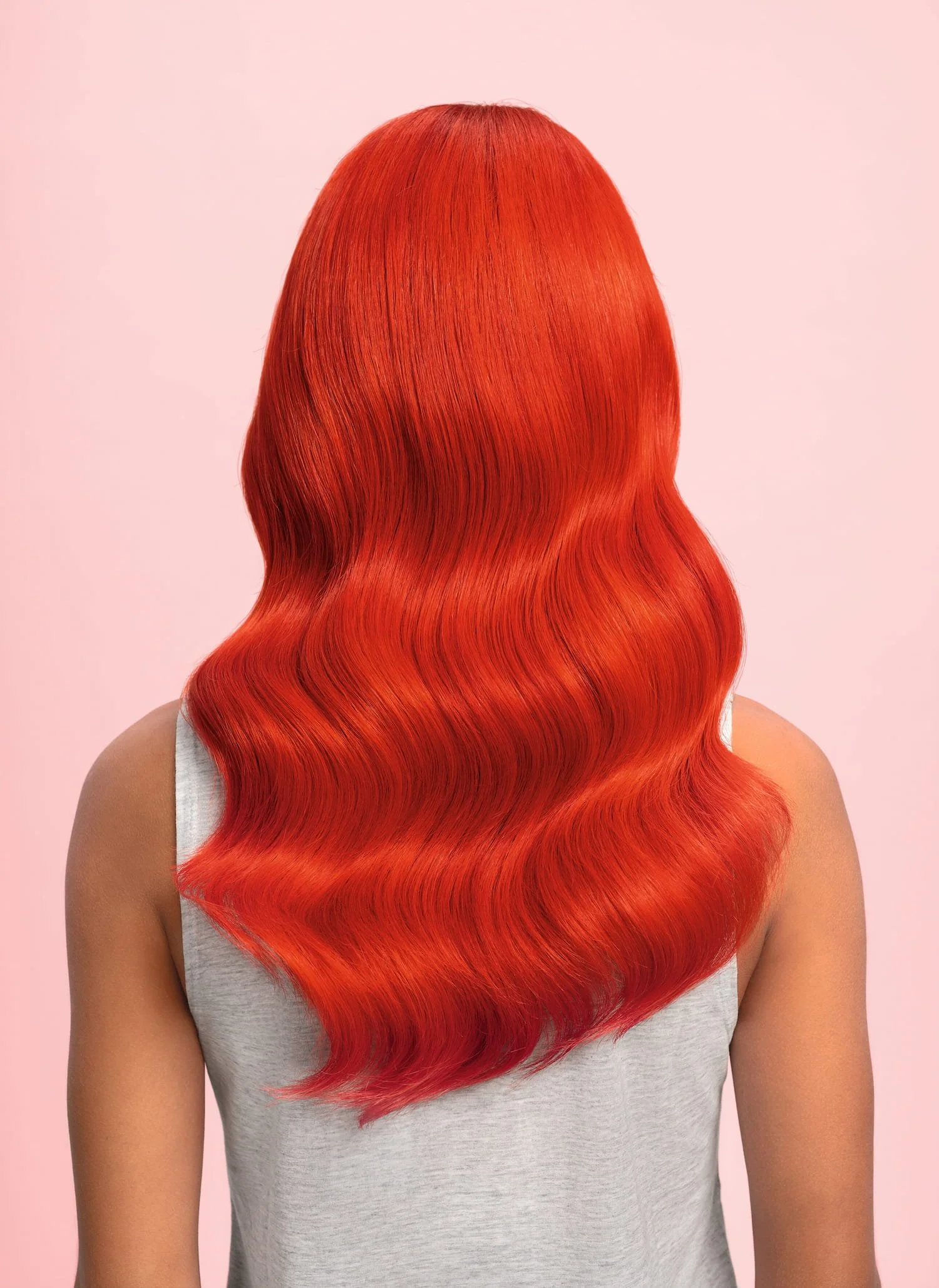 Back view of a person with long, wavy, bright orange-red hair against a light pink background.