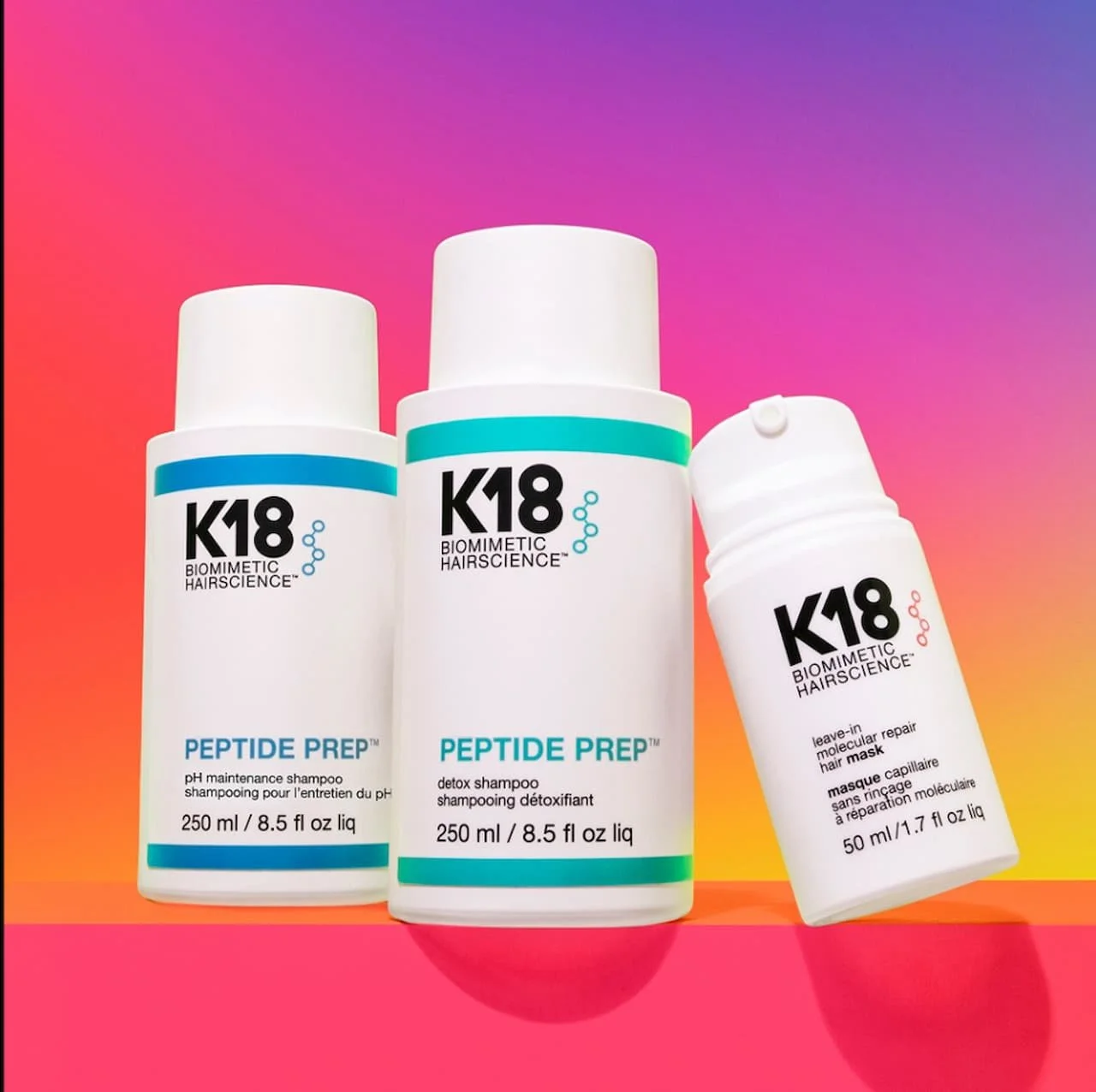 Three bottles of K18 Biometric Hair Science hair care products, including Peptide Prep pH maintenance shampoo, Peptide Prep detox shampoo, and a leave-in molecular repair hair mask, placed on a pink and purple gradient background.