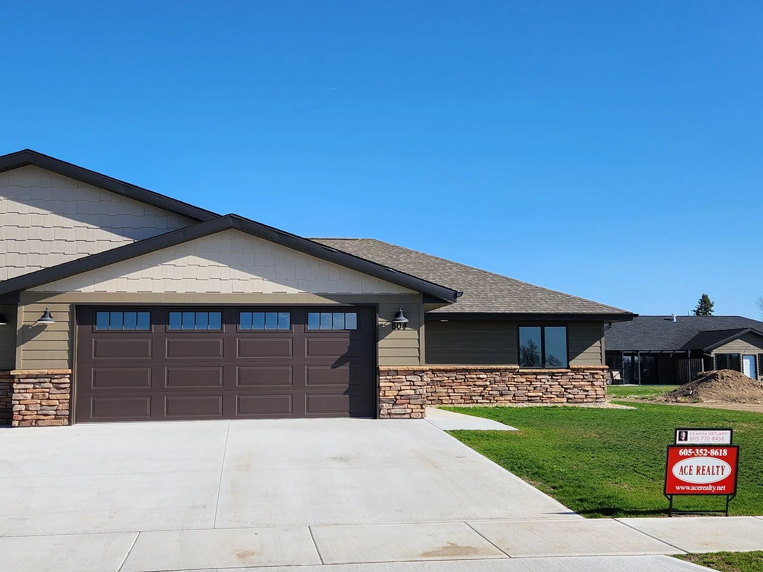 Newley built, single-story house with a brown garage door, brick and siding exterior, green lawn, and a 'For Sale' sign from Ace Realty in the front yard.