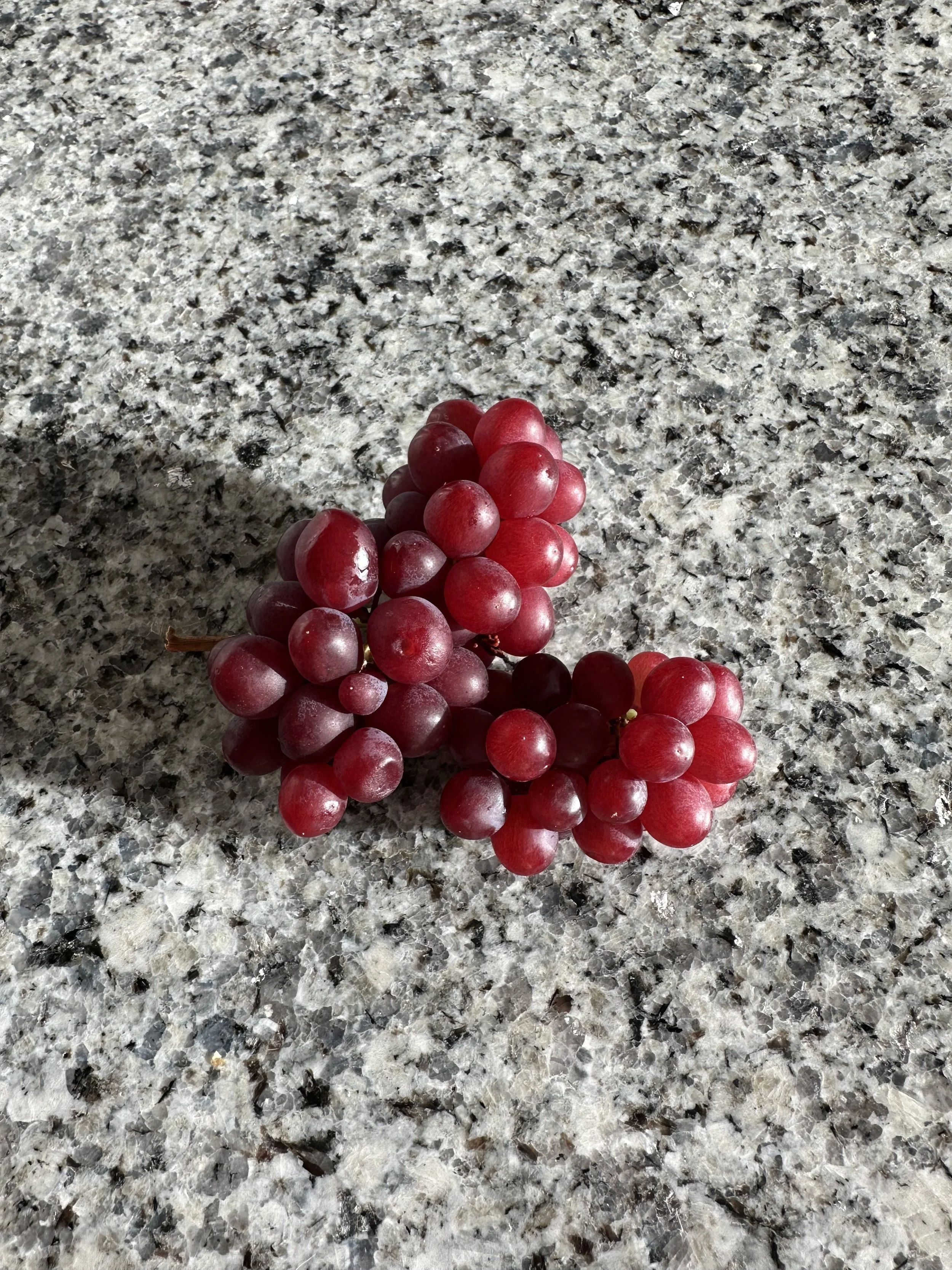 A bunch of red grapes on a speckled gray and white granite surface.