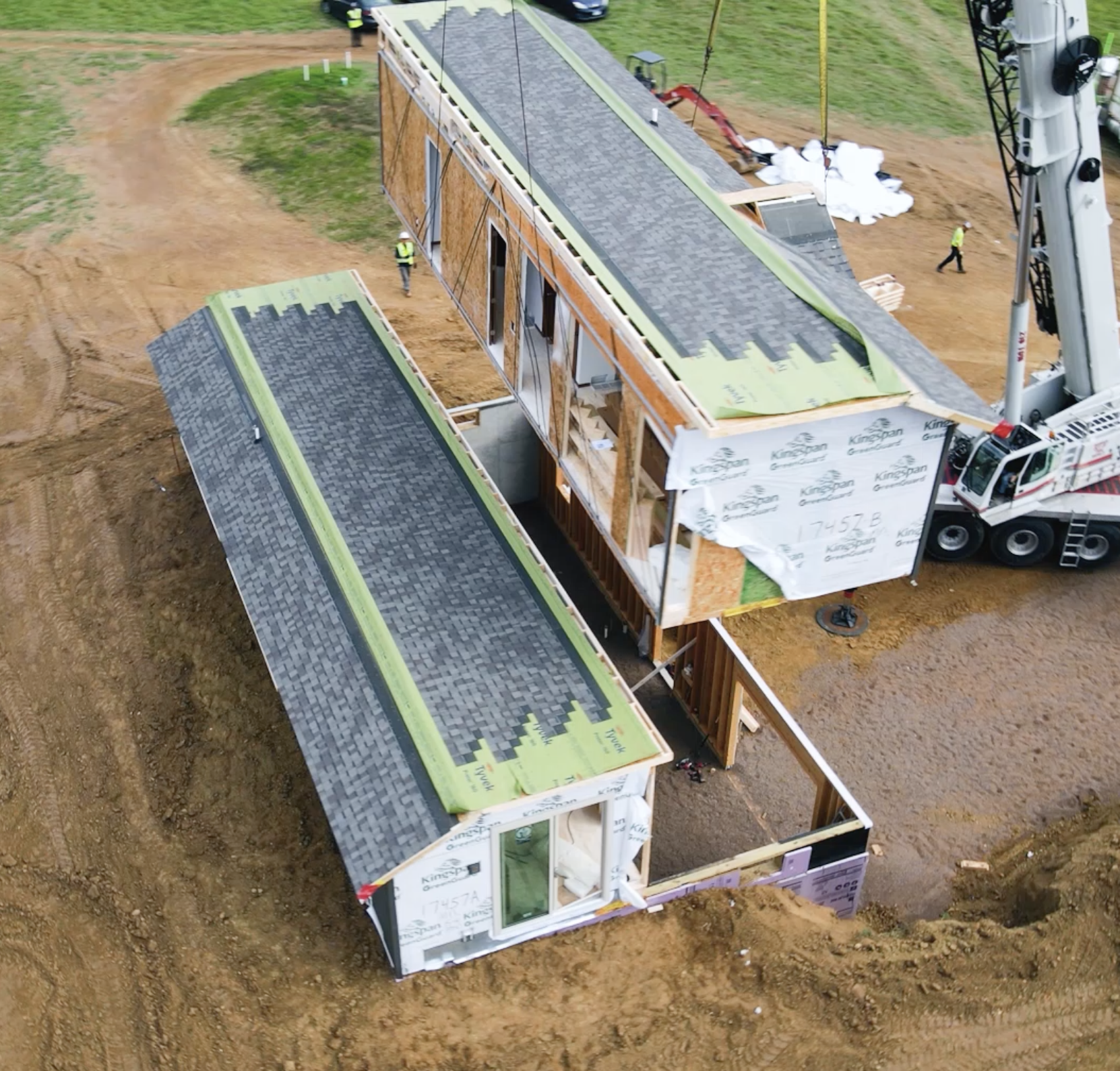Crane placing house section next to first section on foundation at a construction site
