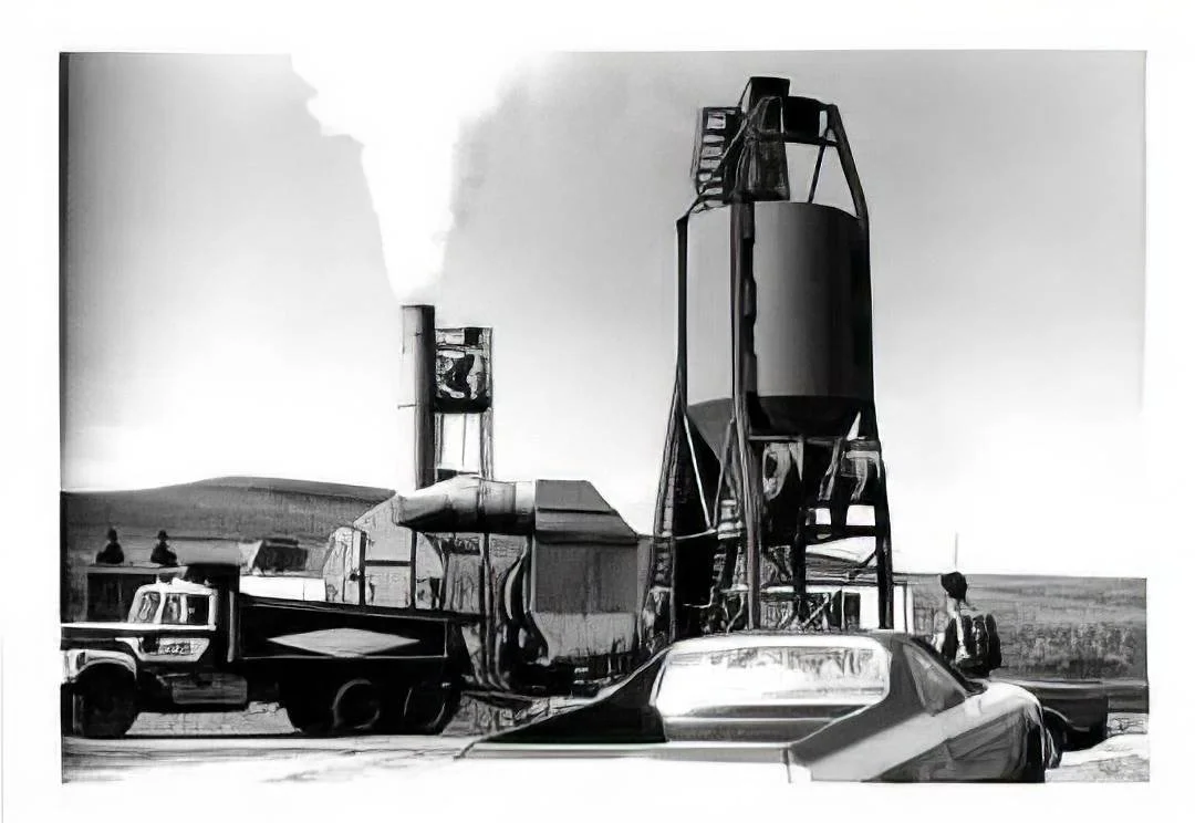 Black and white photo of industrial equipment with a tall silo, a truck, and a parked car in the foreground, and a few people standing nearby.