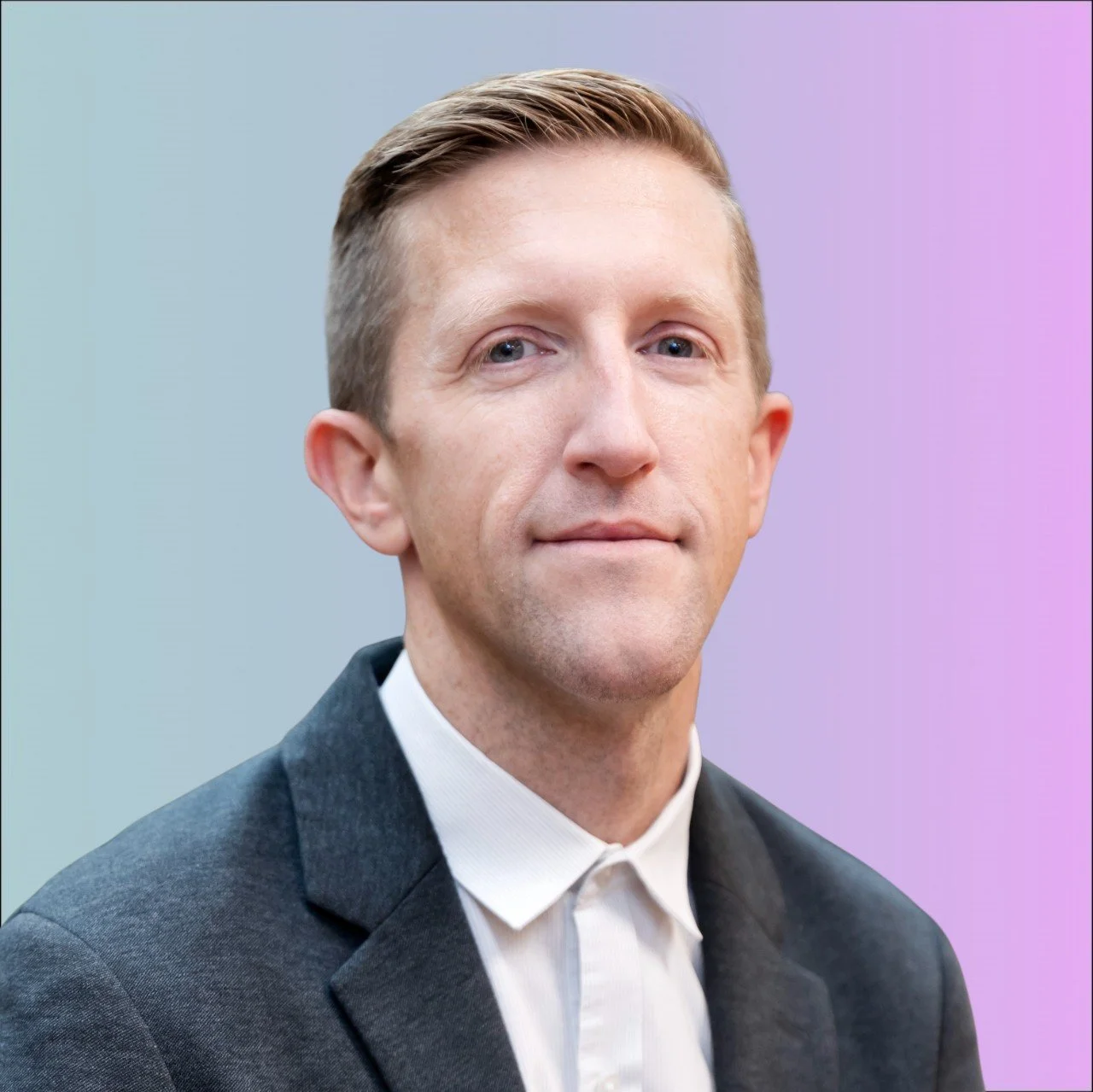Portrait of a man with short light brown hair, wearing a dark blazer and white shirt, against a plain white background.