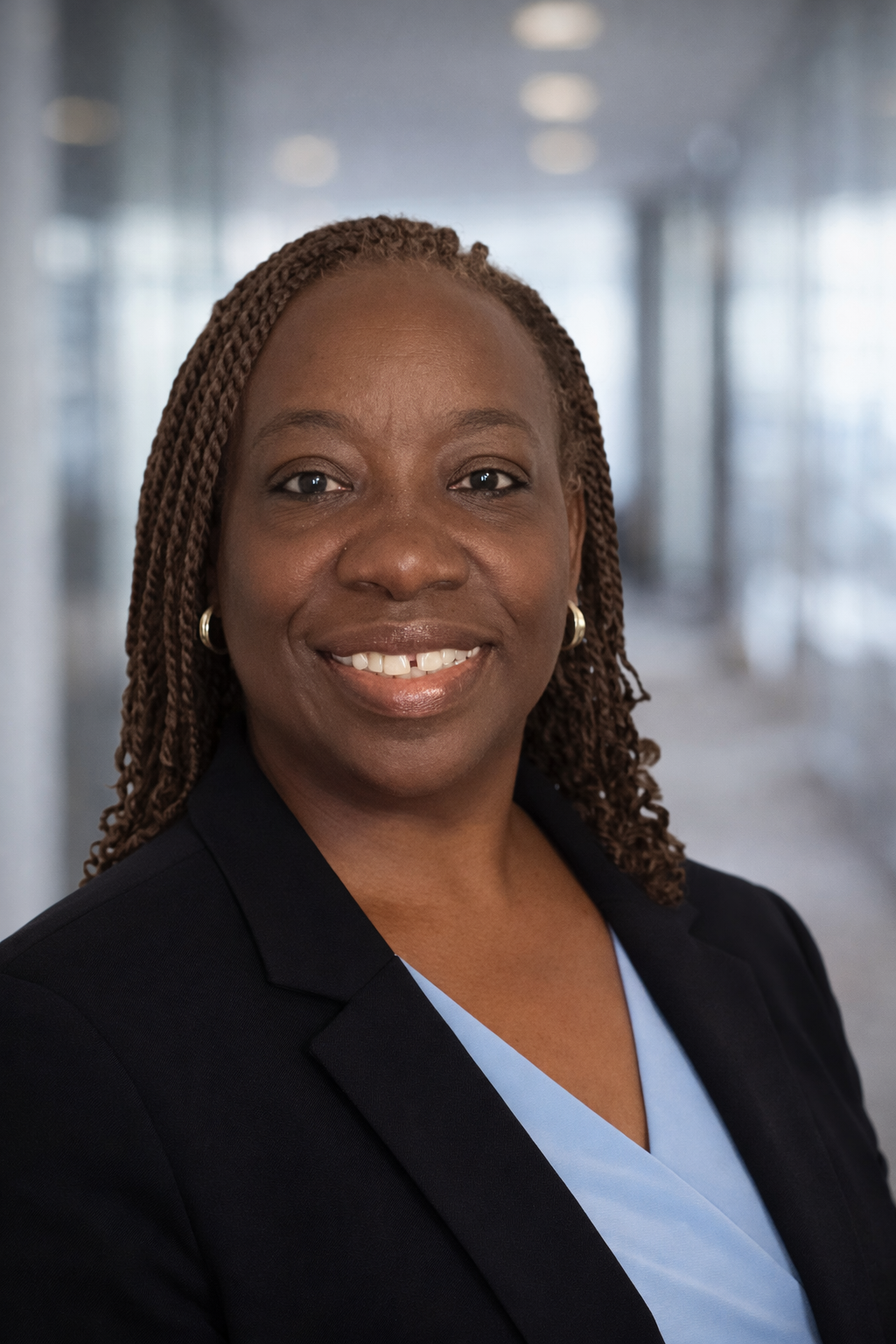 Close-up of a woman with black, wavy hair wearing a pink top, smiling slightly.