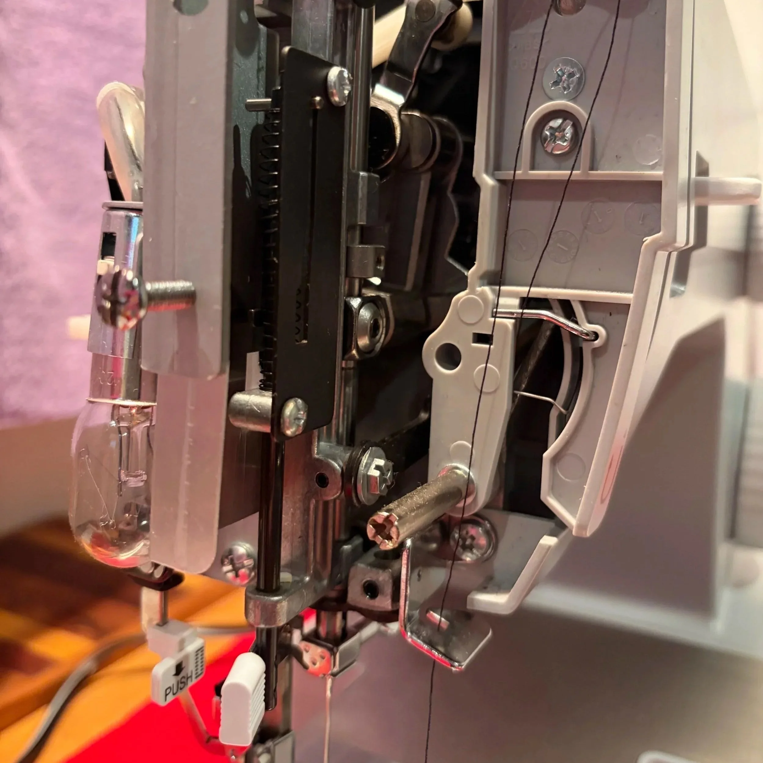 Close-up view of the internal mechanical components of a sewing machine, showing metal parts, screws, and a tension wire.
