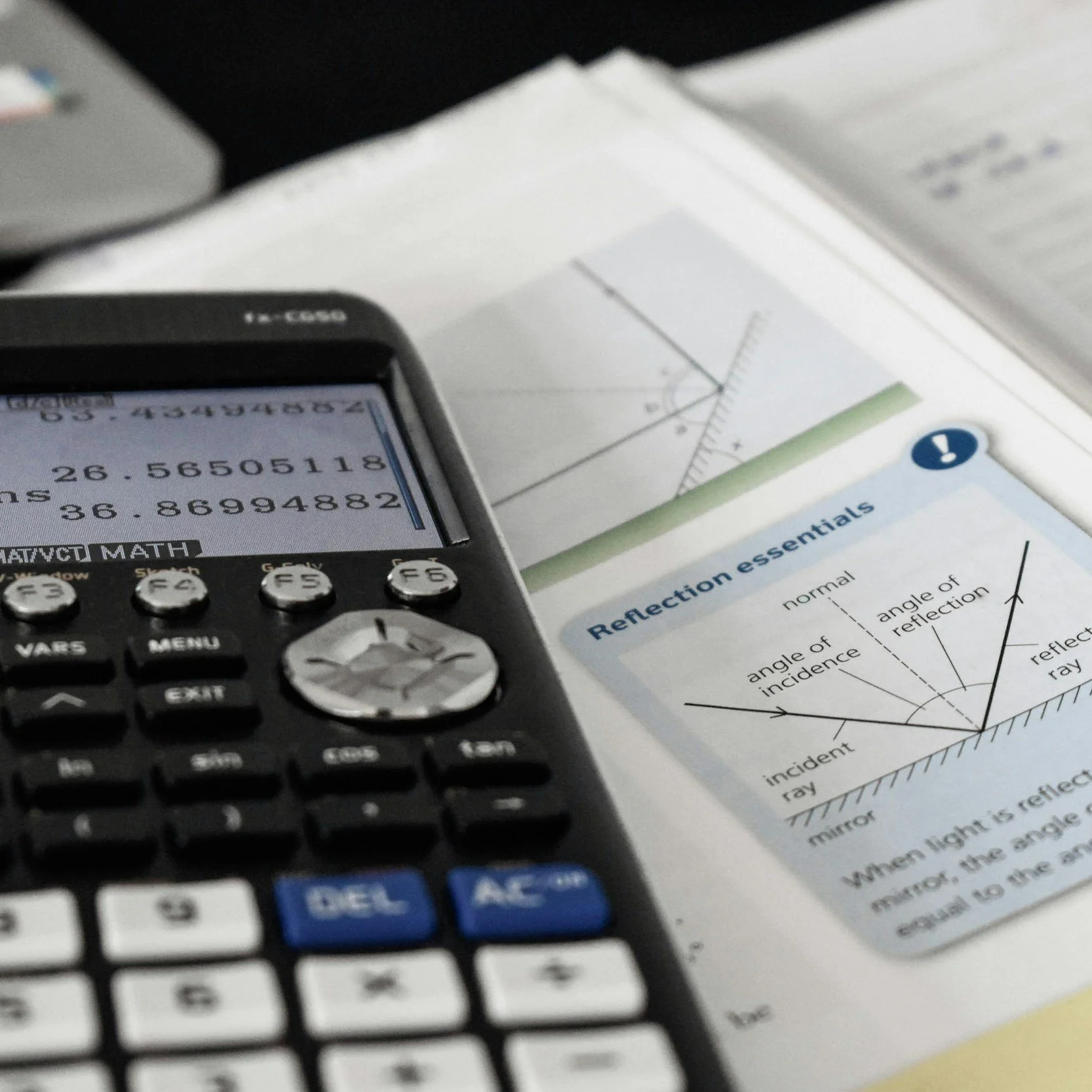 A TI-84 calculator displaying a math calculation, with an open textbook page about reflection principles and a graph in the background.