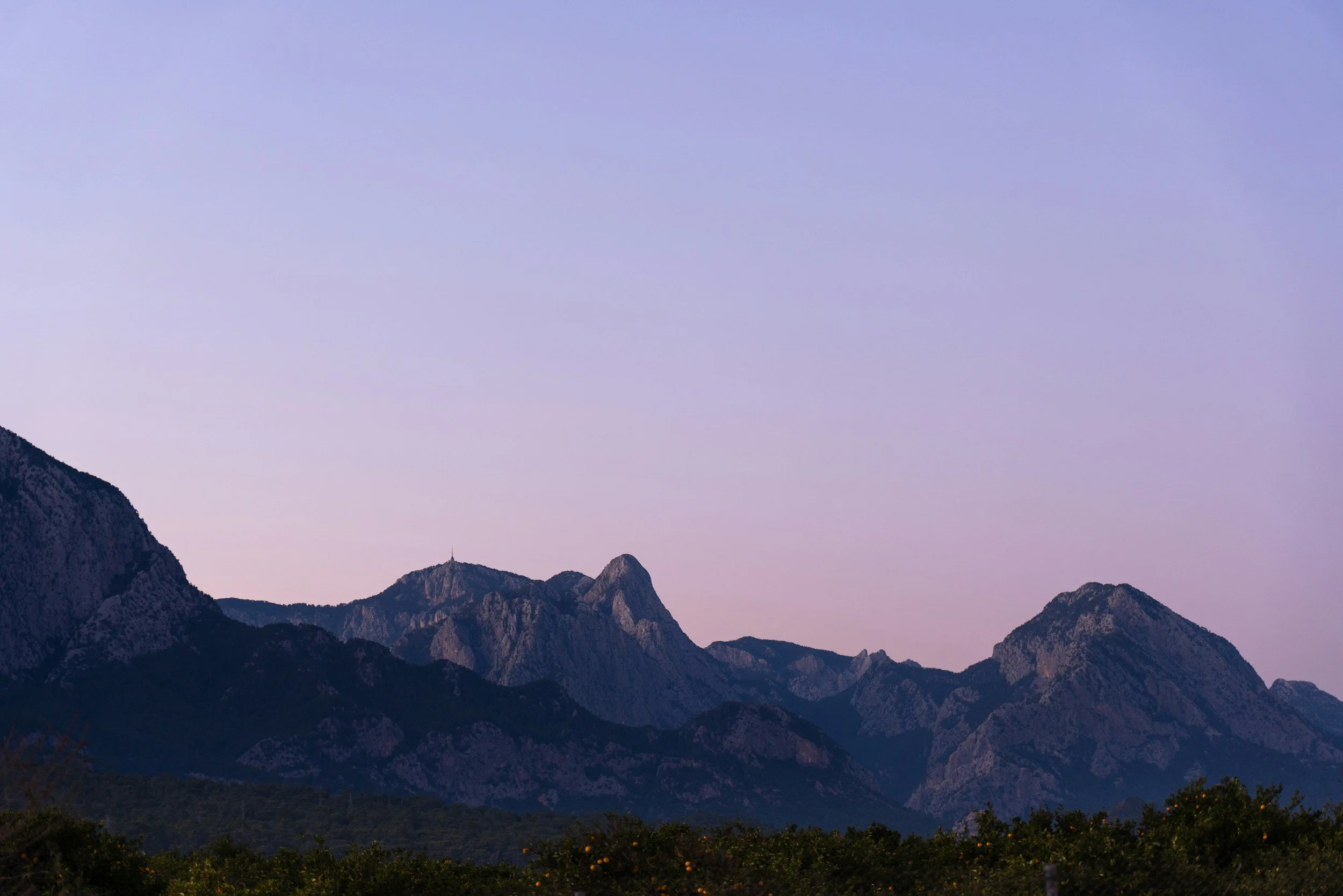A modern house on a grassy hillside with snow-capped mountains in the background under a cloudy sky.