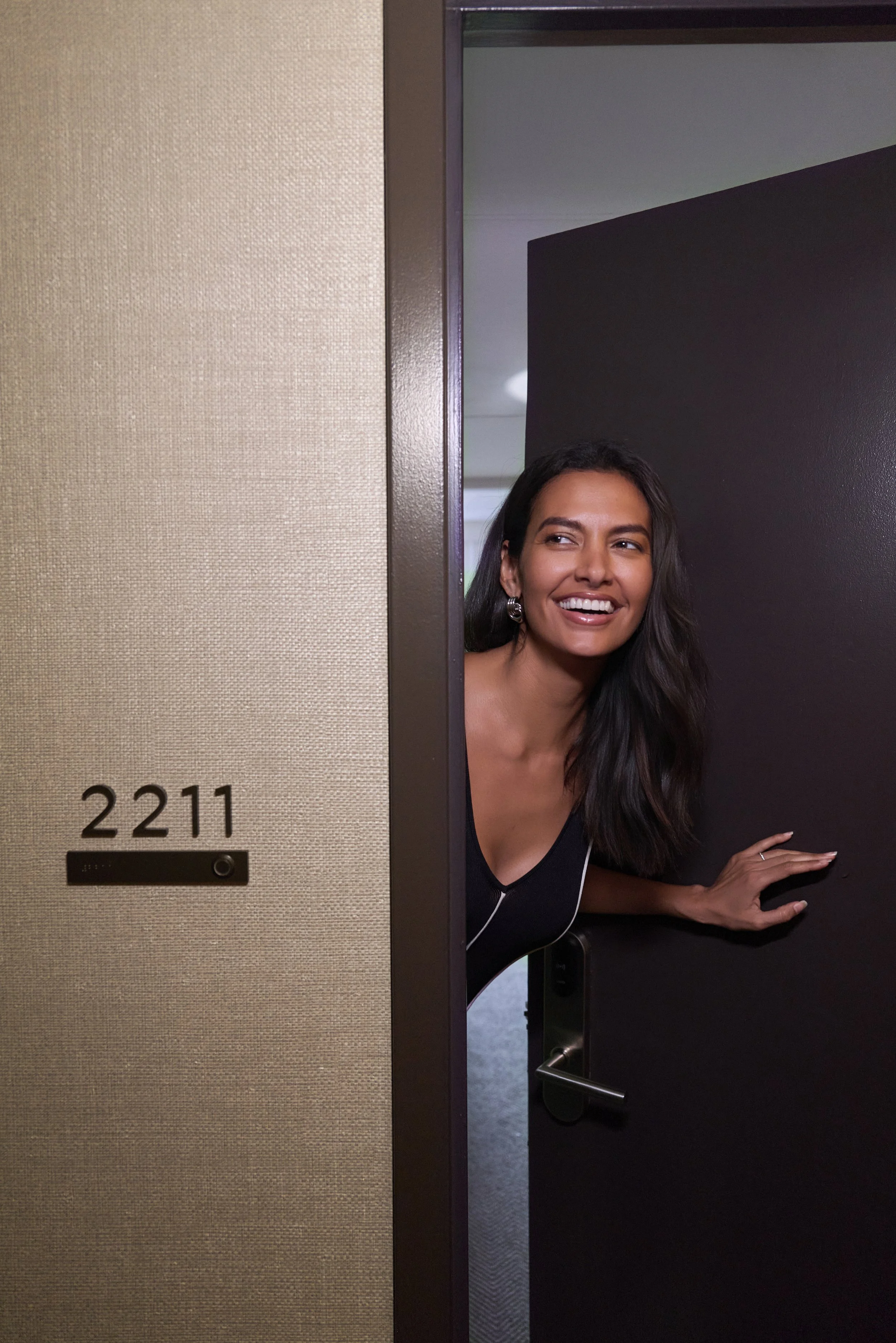 A woman peeking out from behind a partially open door, smiling.