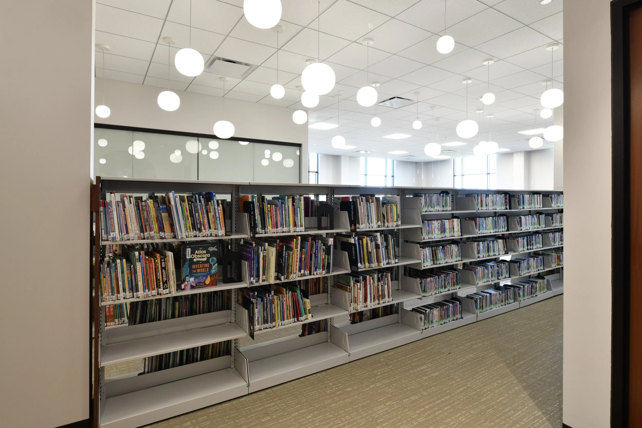 Bookshelves filled with books in a modern library with bright lighting and large windows.