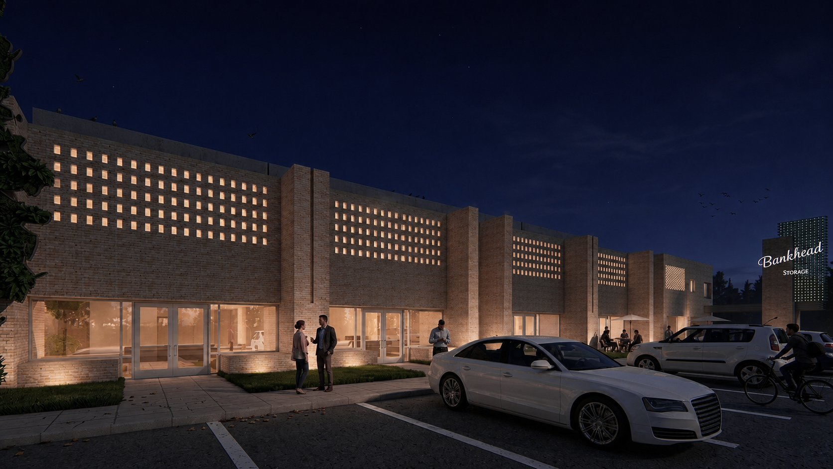 Night view of a modern brick commercial building with illuminated square windows, people chatting outside, parked cars, and a sign that reads 'Bankhead Storage'.