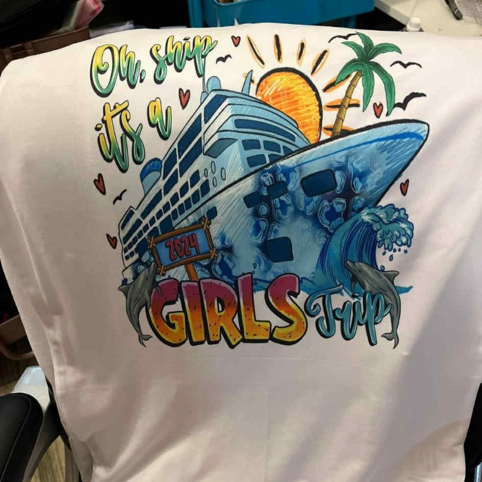 Colorful illustration of a cruise ship with dolphins, a palm tree, ocean waves, and a sunset. Text reads 'Oh, ship it’s a GIRLS trip 2024' with hearts and seagulls.