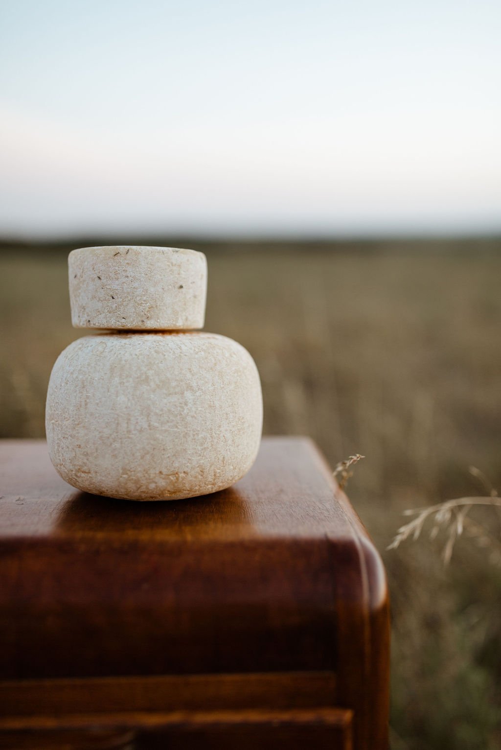 Stacked smooth, beige stones on a wooden surface outdoors with a blurred landscape background.
