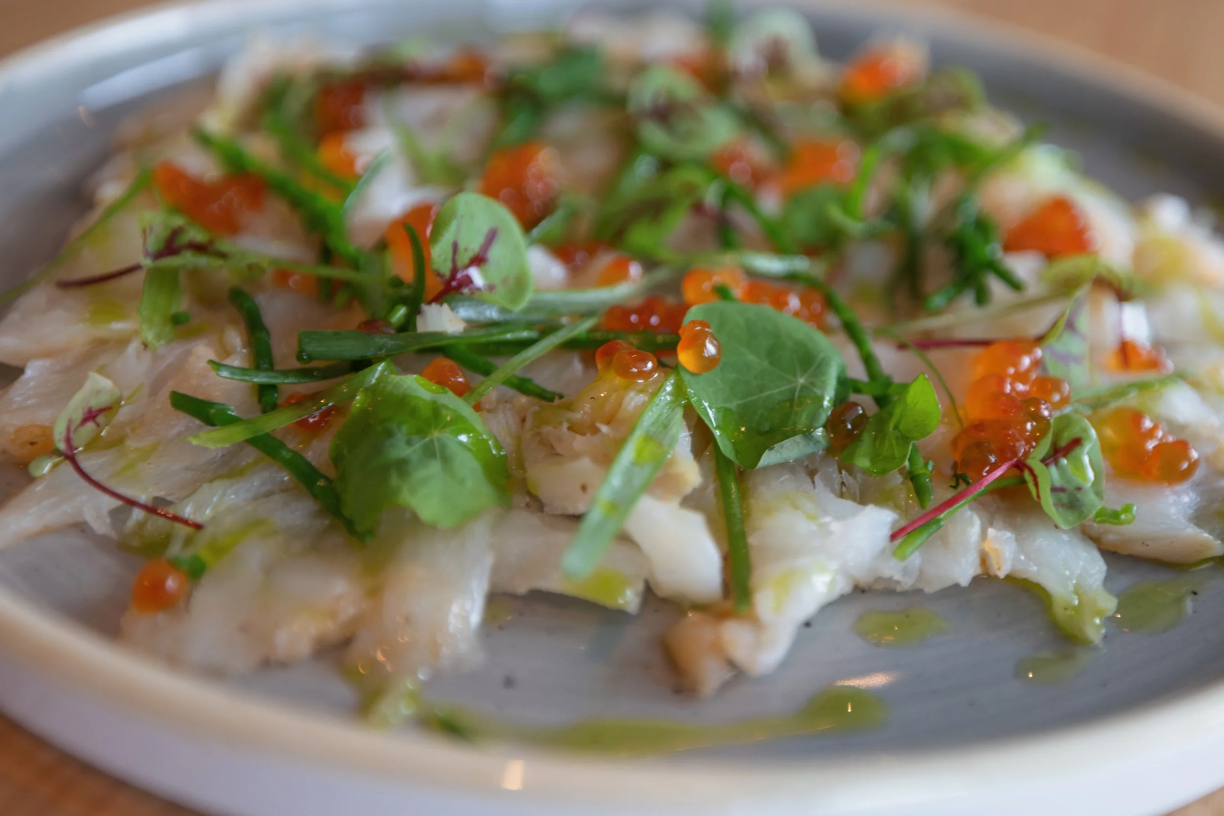 A plate of fish topped with microgreens, orange roe, and drizzled with green sauce.